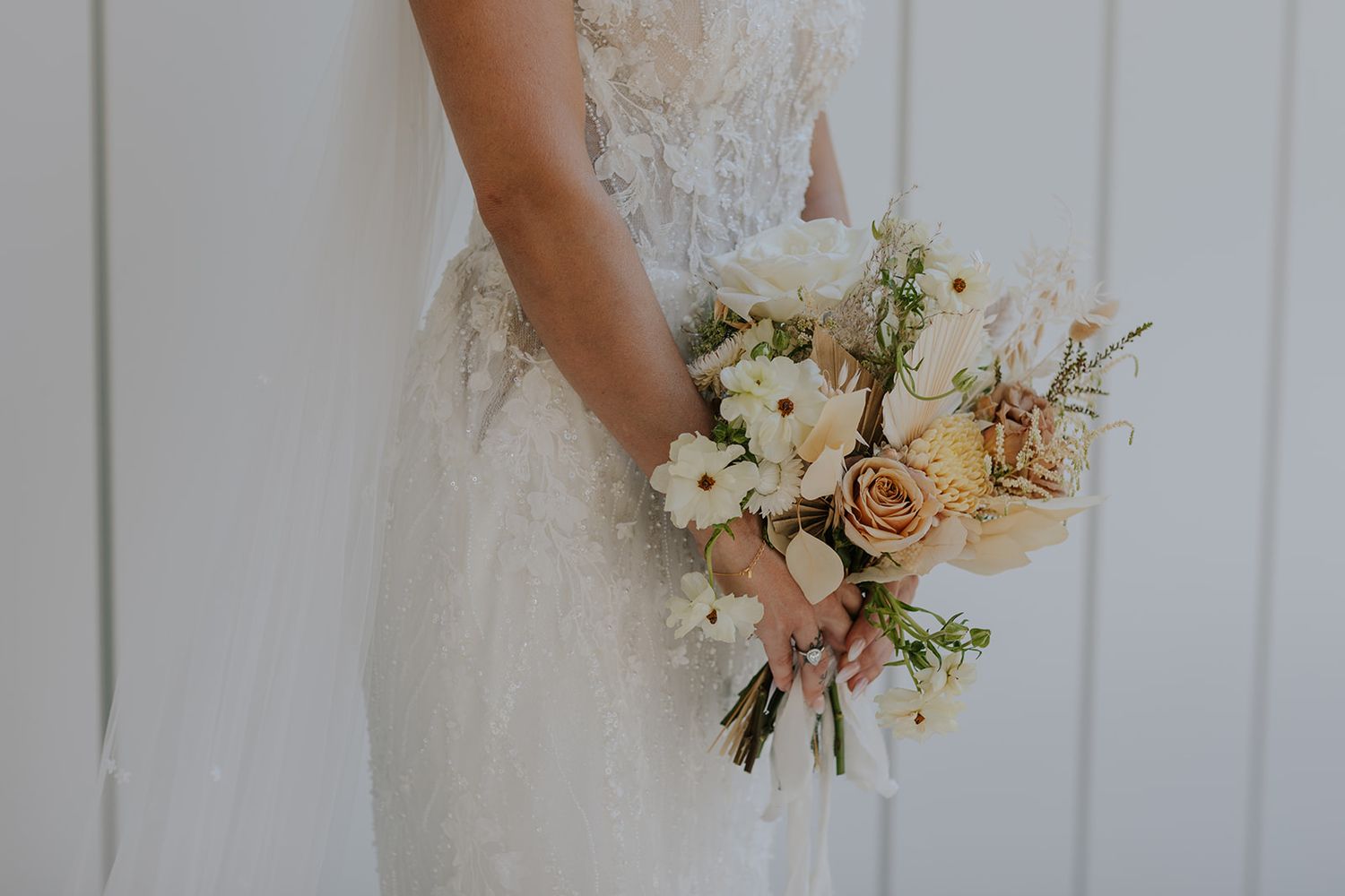 Close-up of bridal bouquet featuring white and blush flowers against white background.