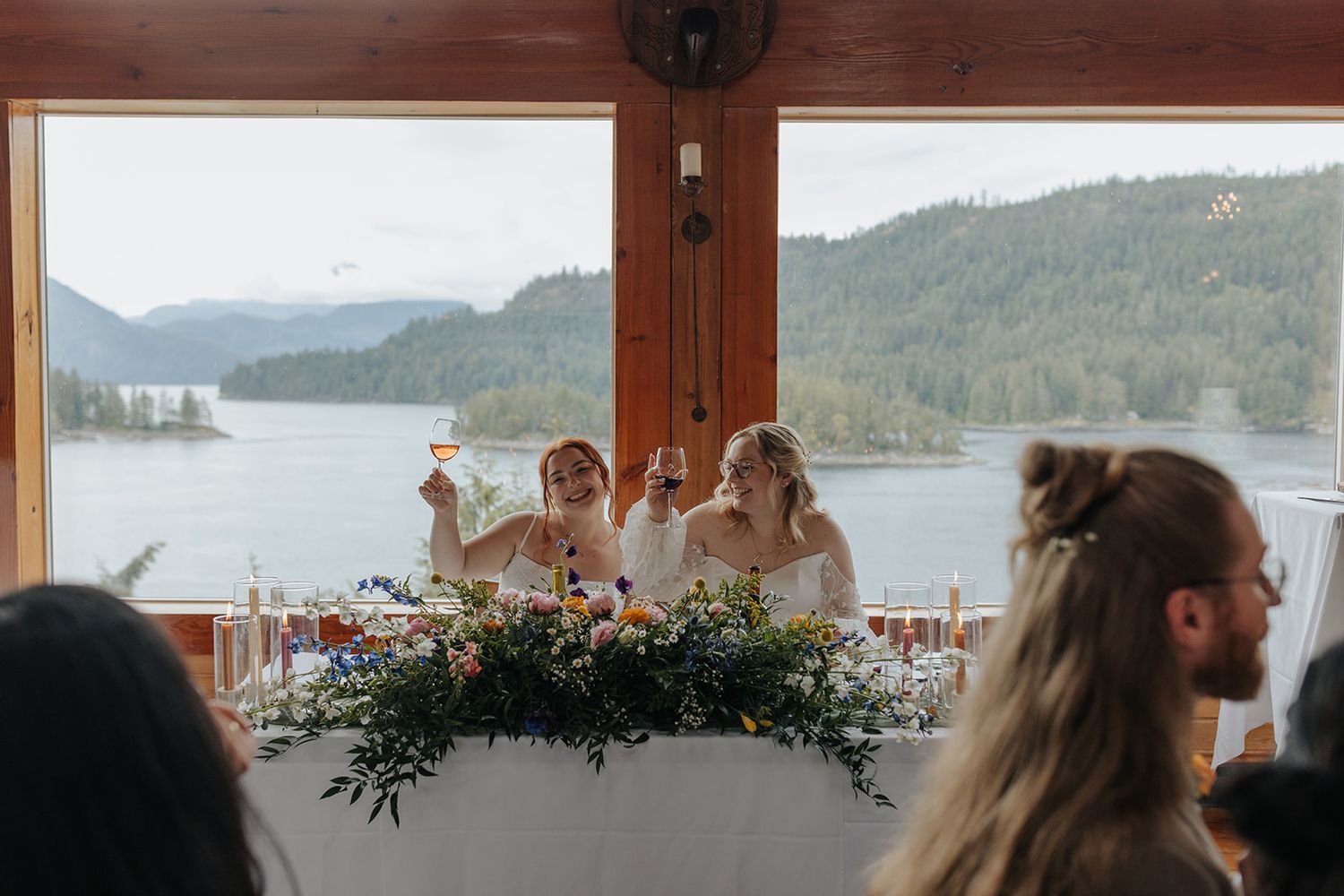 Elegant wedding reception venue with mountain lake views through large windows and rustic wooden interior.