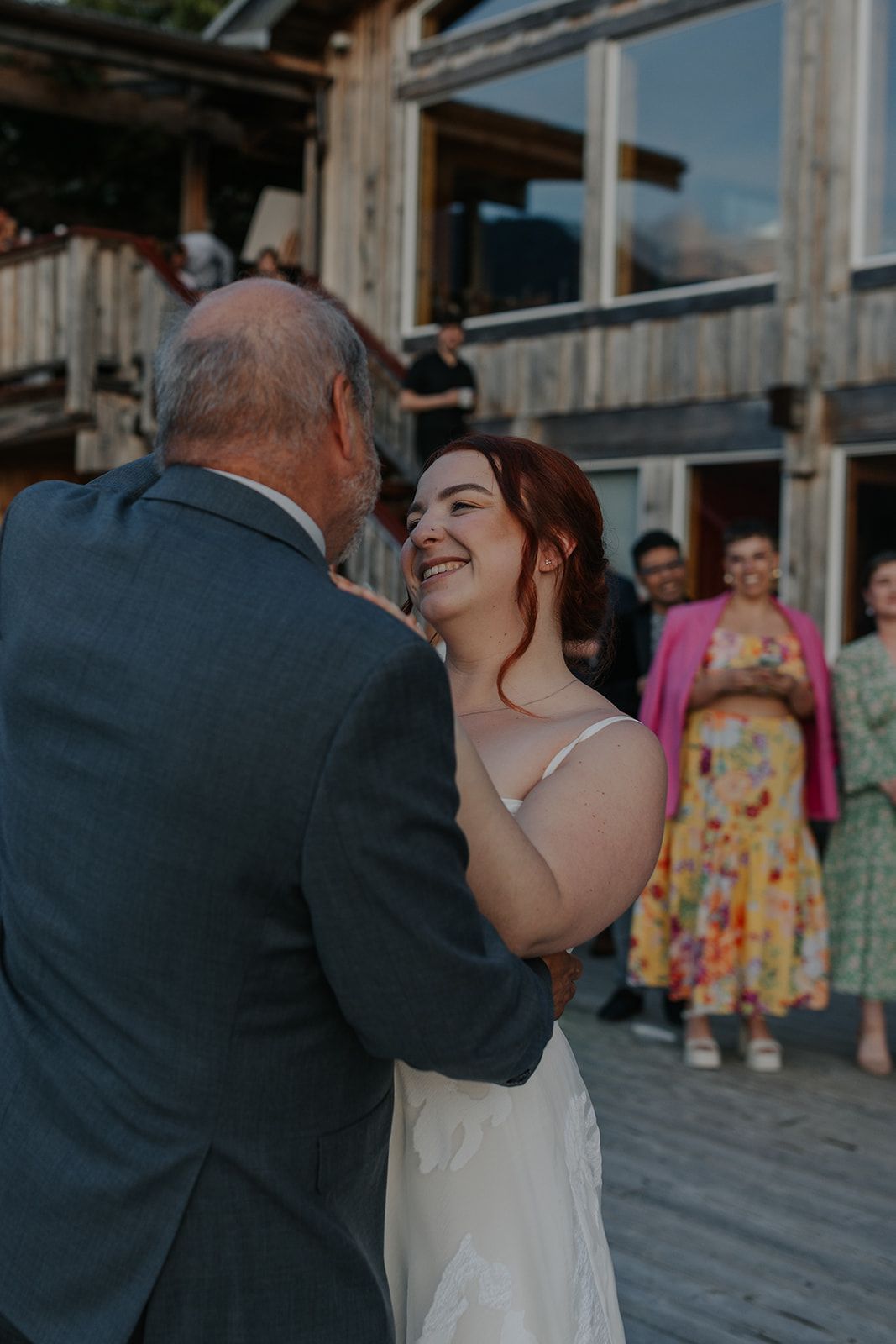 Wedding dance on a rustic wooden deck with guests watching in the background.