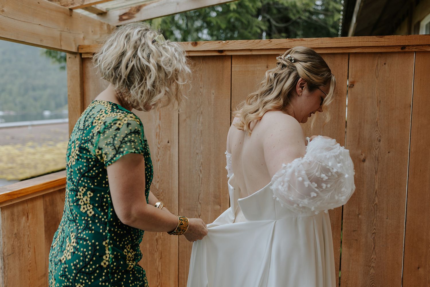 Wedding dresses hanging on wooden fence with green foliage in background.