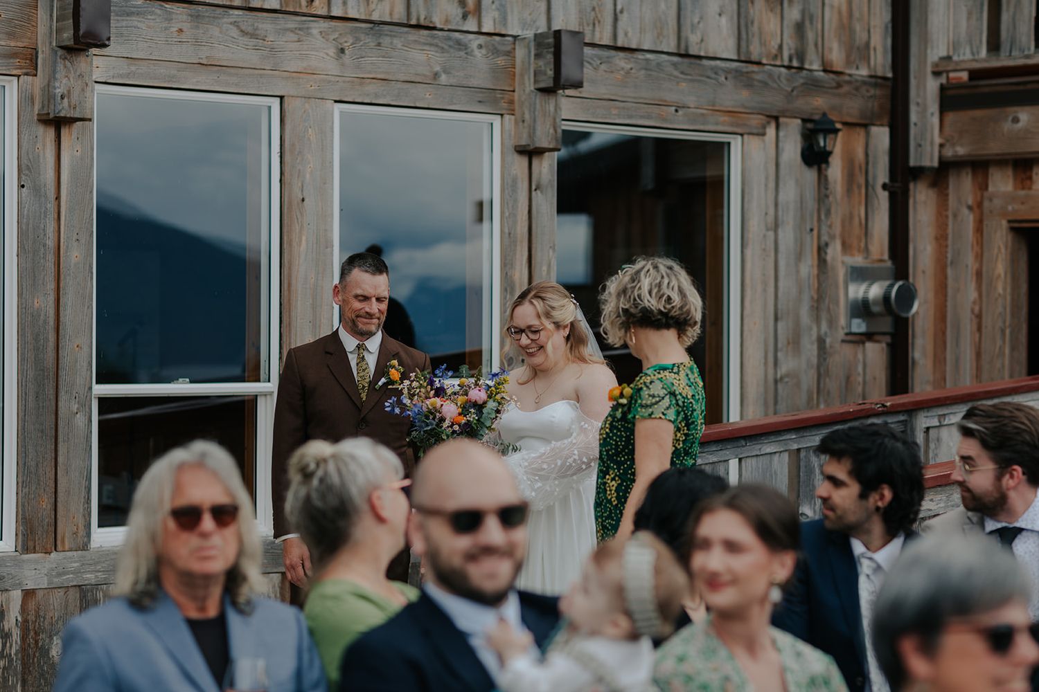 Wedding guests mingling on rustic wooden deck with mountain views.