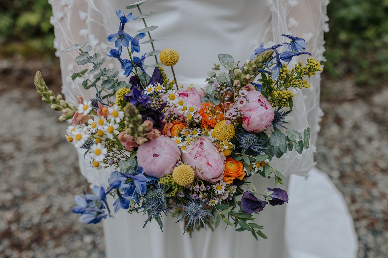Colorful wedding bouquet featuring blue, pink, and yellow flowers with greenery accents.