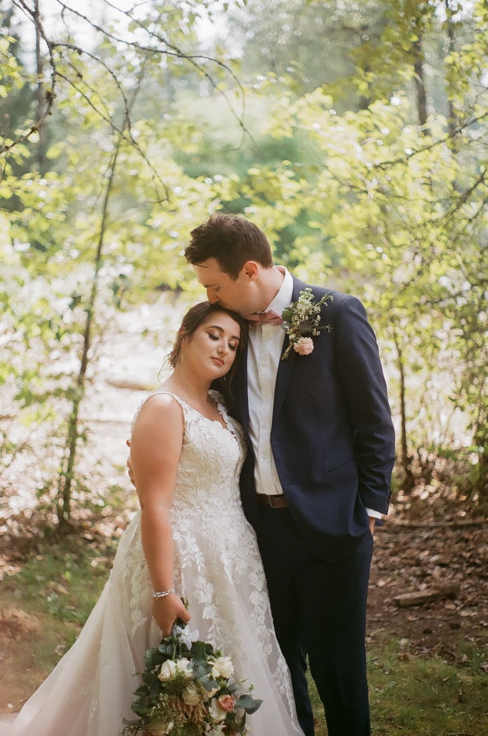 A tender wedding moment captured in a sunlit forest setting.