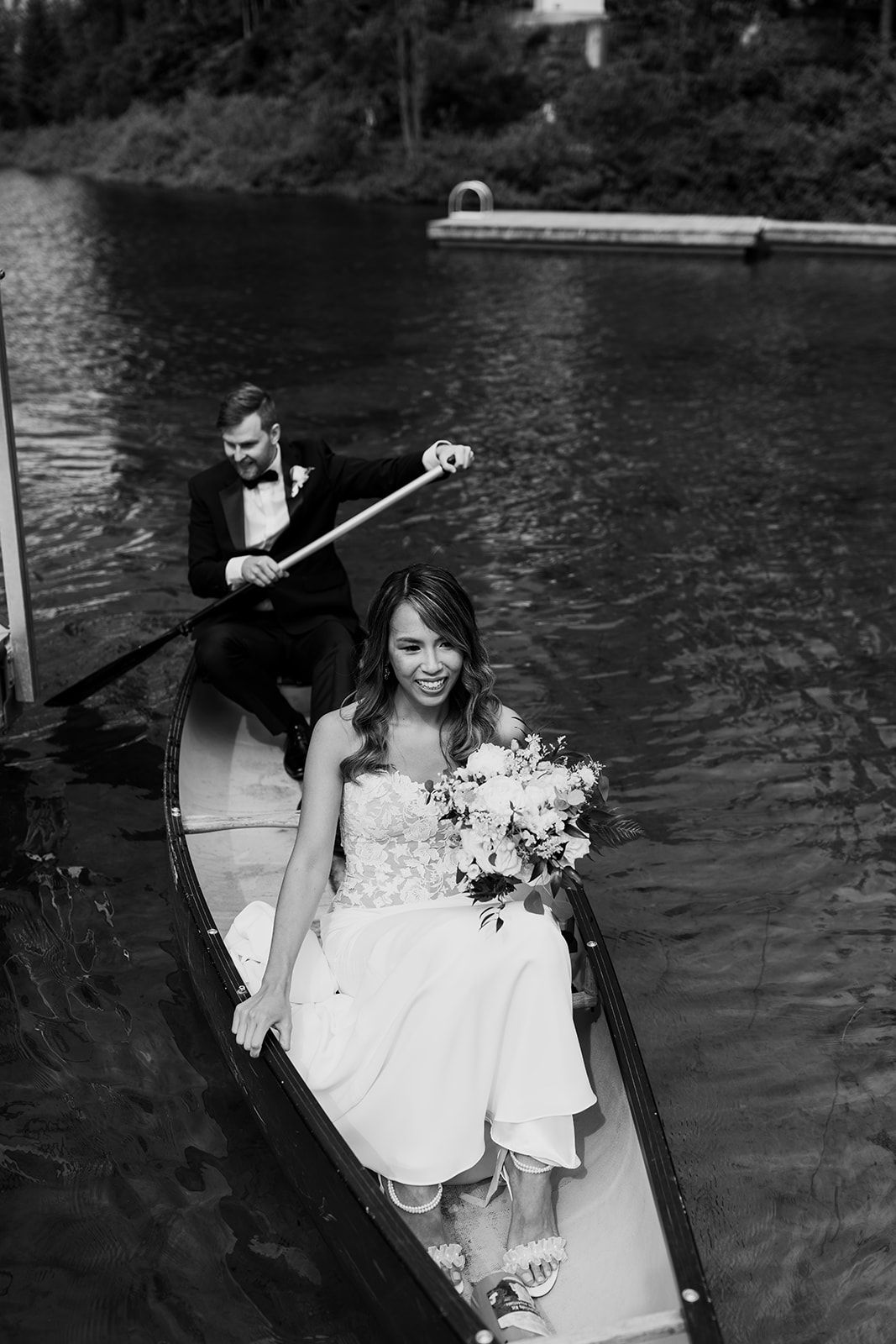 Black and white photo of couple in a canoe on a lake with wedding attire.