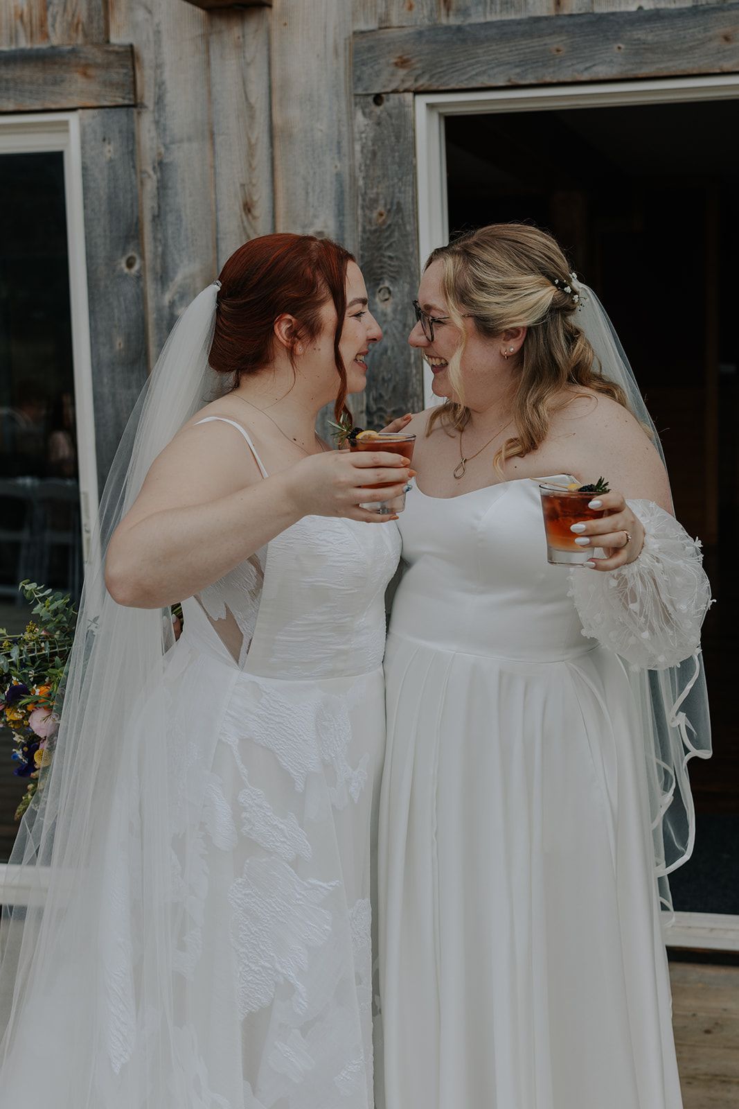 Two people in white wedding dresses share an intimate moment.