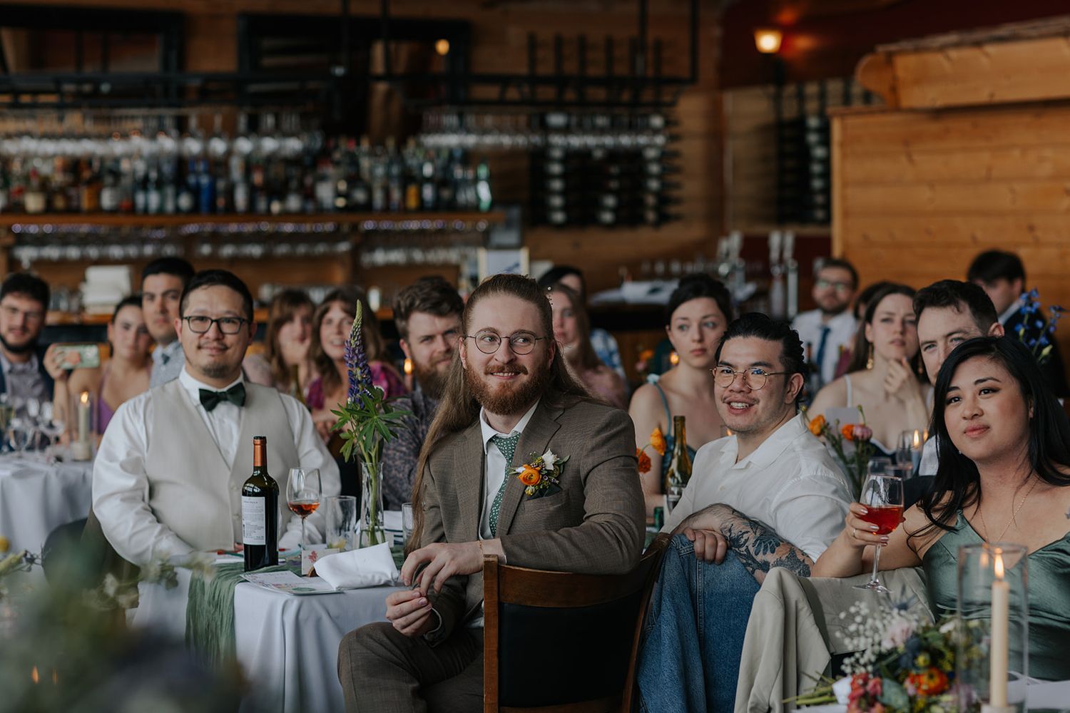 Wedding reception guests enjoy entertainment at rustic venue with wine glasses.
