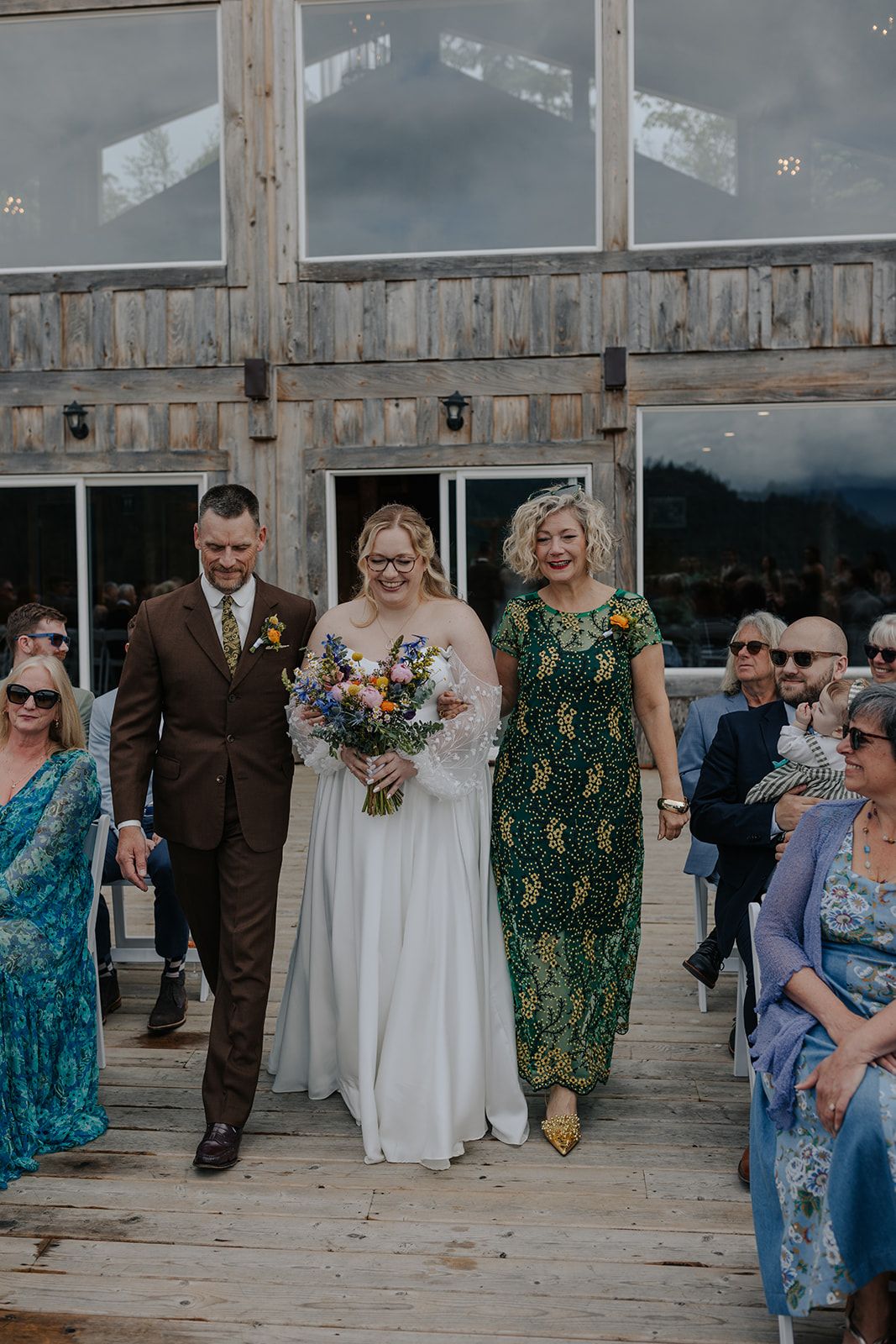 Wedding party processional on rustic deck with dramatic mountain backdrop.