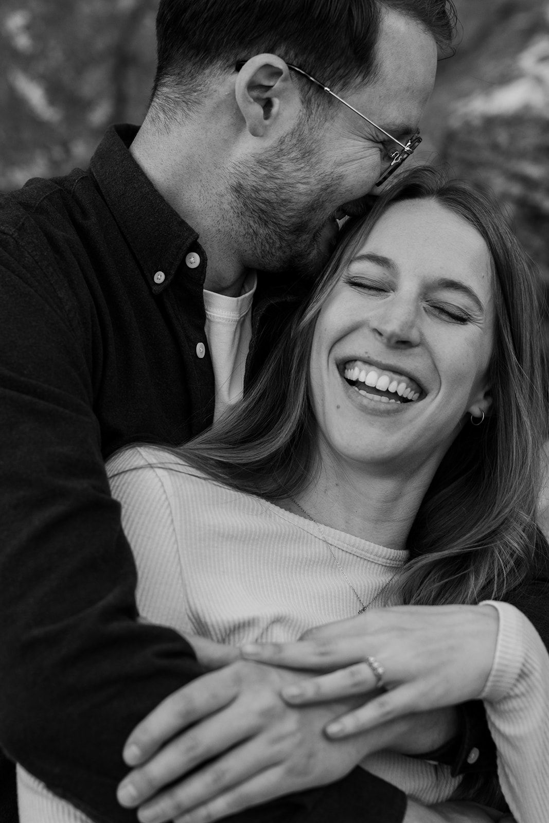 A couple shares an intimate moment of laughter and affection in a close-up black and white photo series.