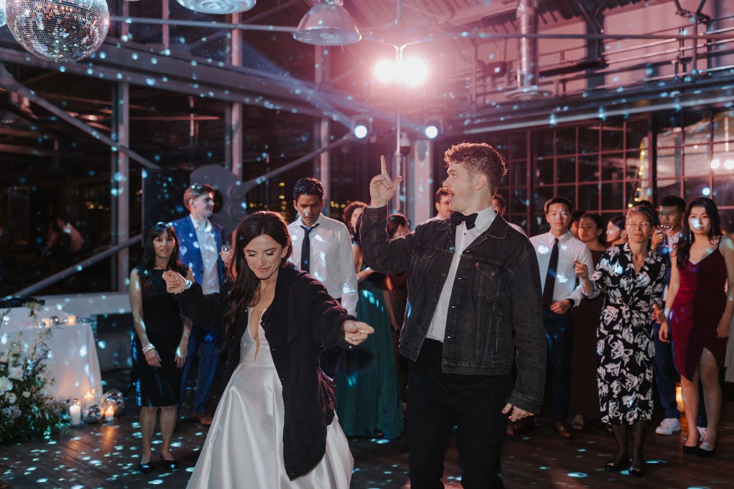 Wedding reception dance party with guests celebrating under atmospheric lighting.