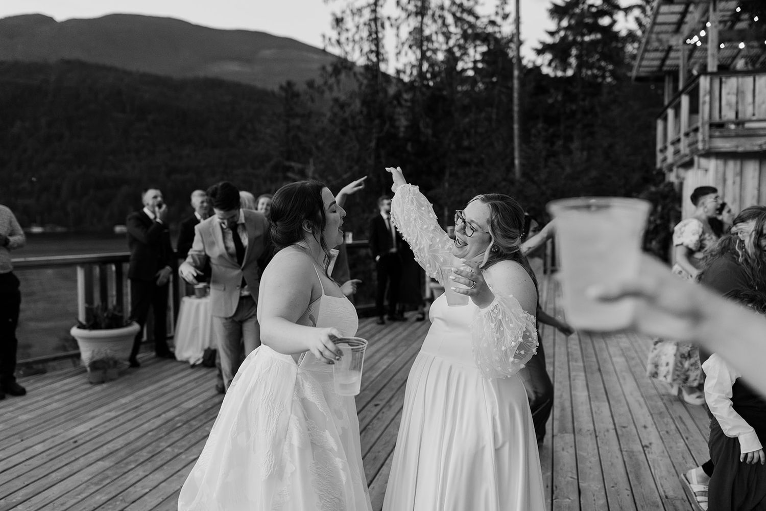 Wedding celebration with dancing guests on a deck against a mountain backdrop.