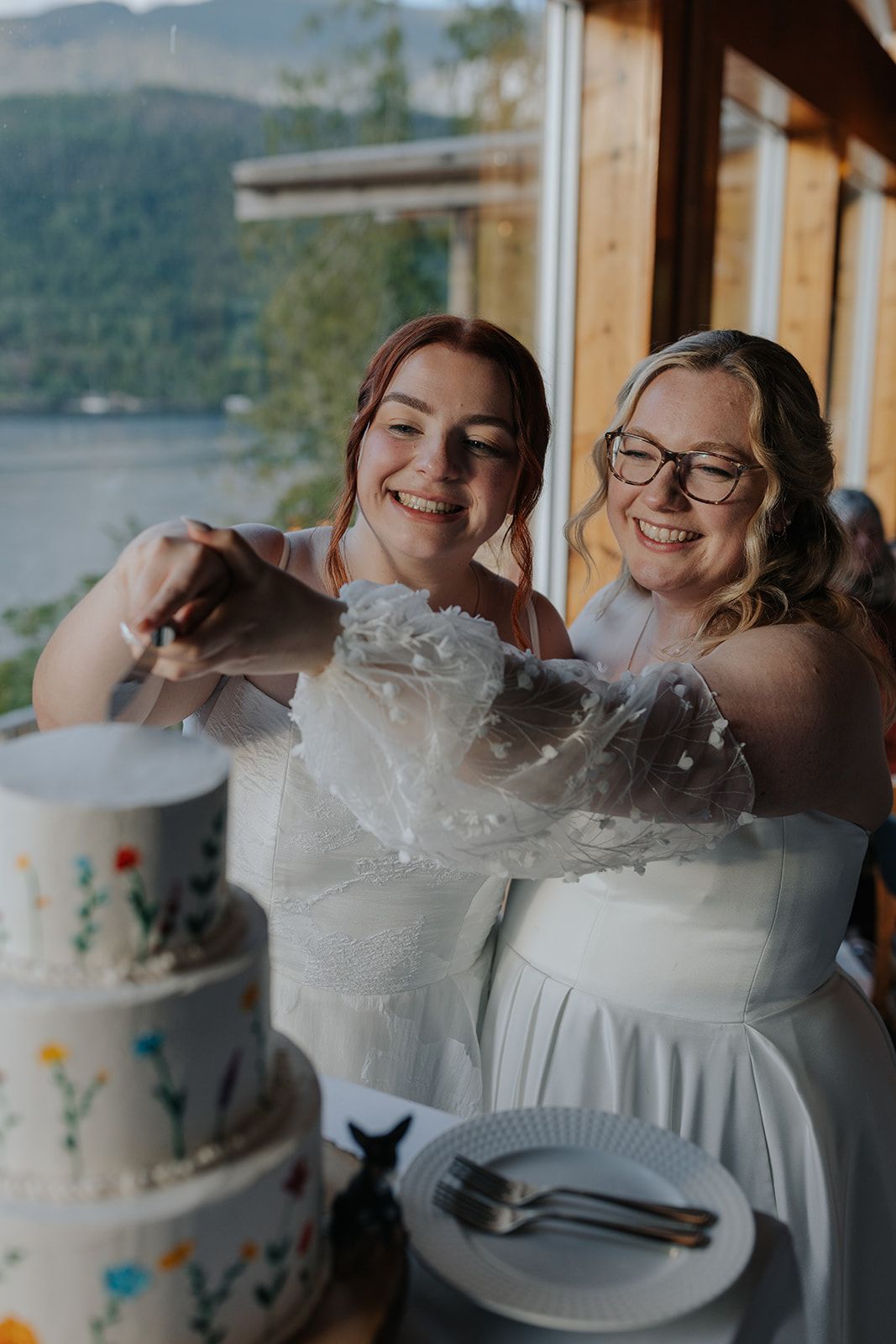 Wedding couple sharing cake and laughter during their reception with mountain views in background.