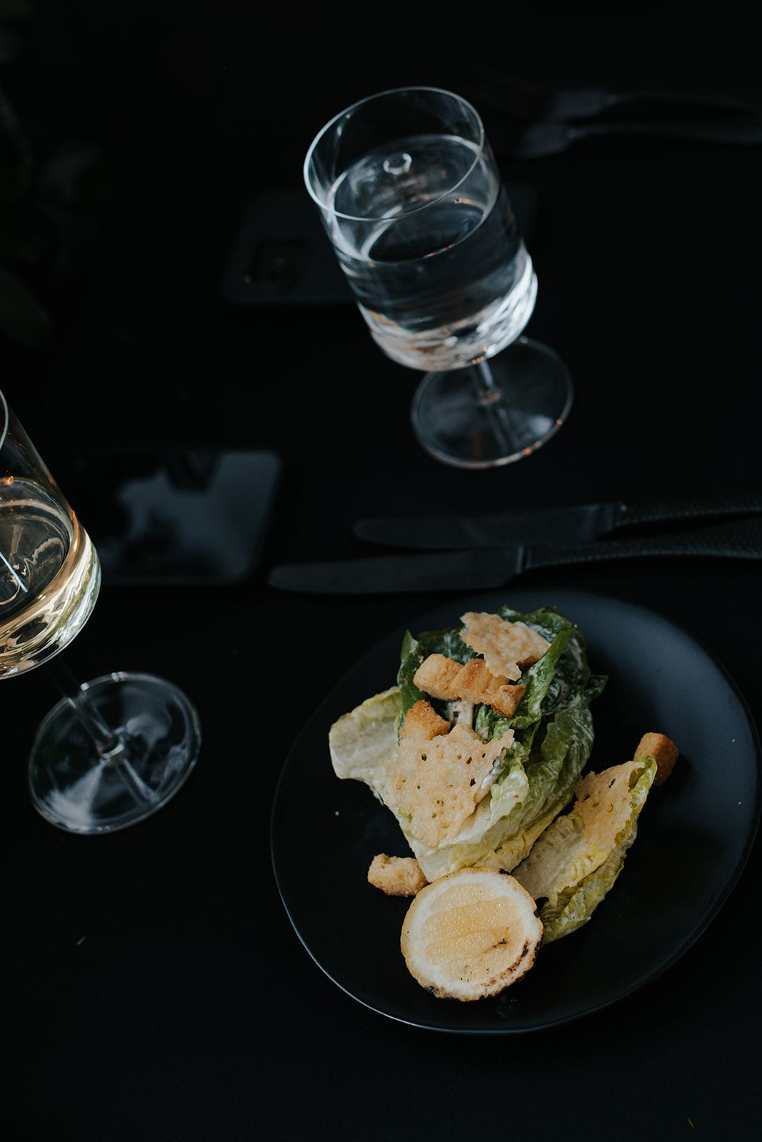 Elegant plated dinner with wine glasses on dark table setting.