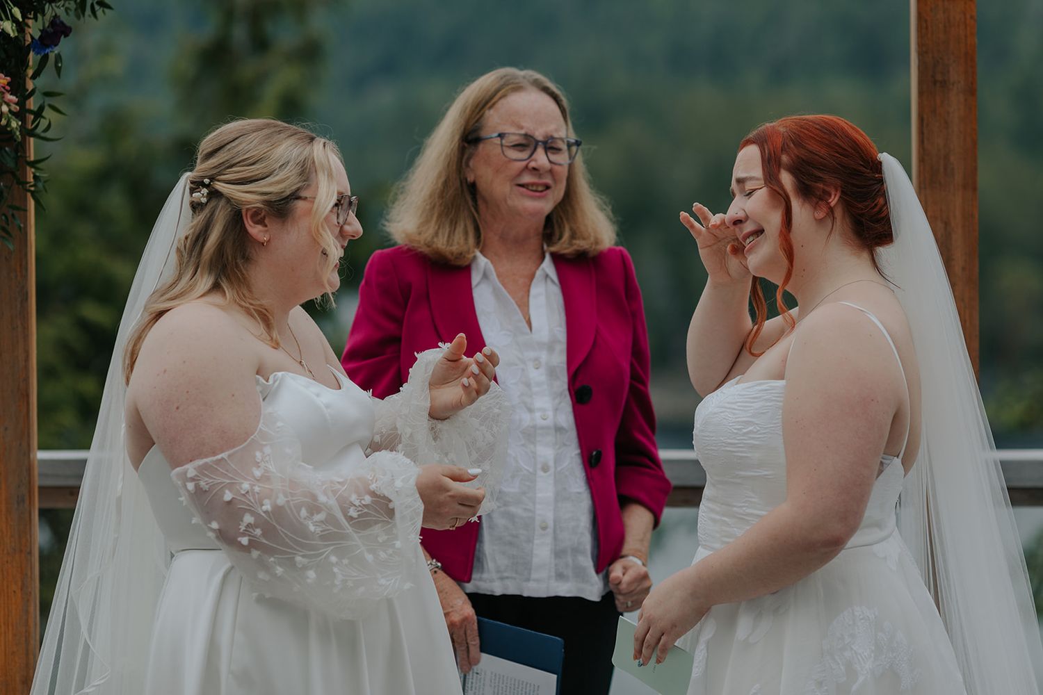 Wedding ceremony taking place under a wooden pergola with mountain views in the background.
