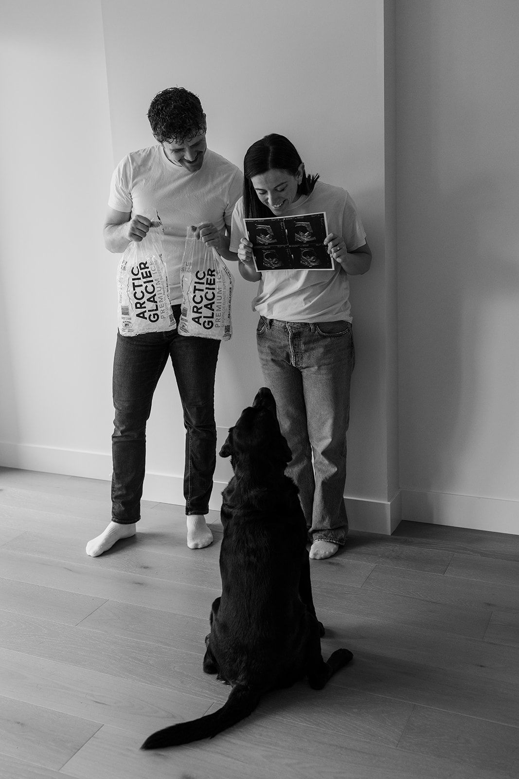 Black and white image of couple reading with their dog sitting attentively in front of them.