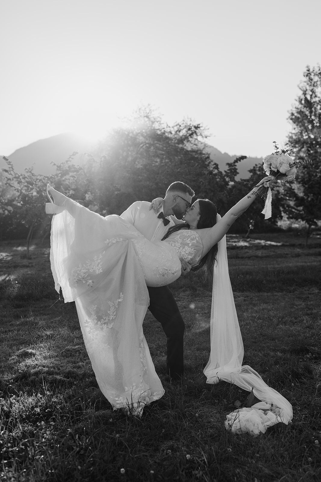 Artistic black and white photo of wedding dress flowing in sunlit field.