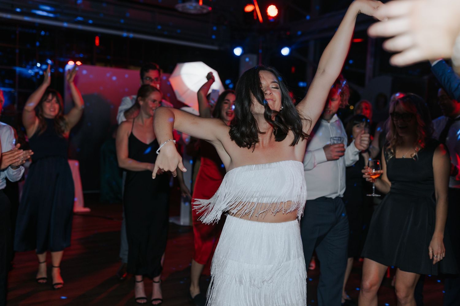 Wedding guests dance and celebrate on a dimly lit dance floor with red lighting accents.