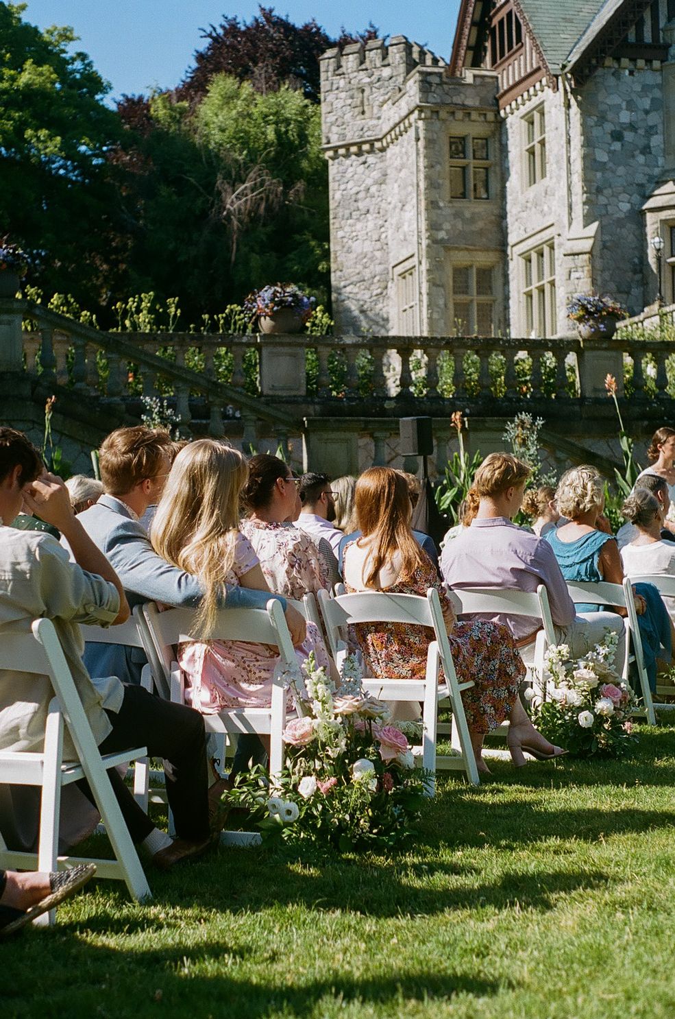 White chairs set up on lawn for outdoor wedding ceremony with stone castle backdrop.