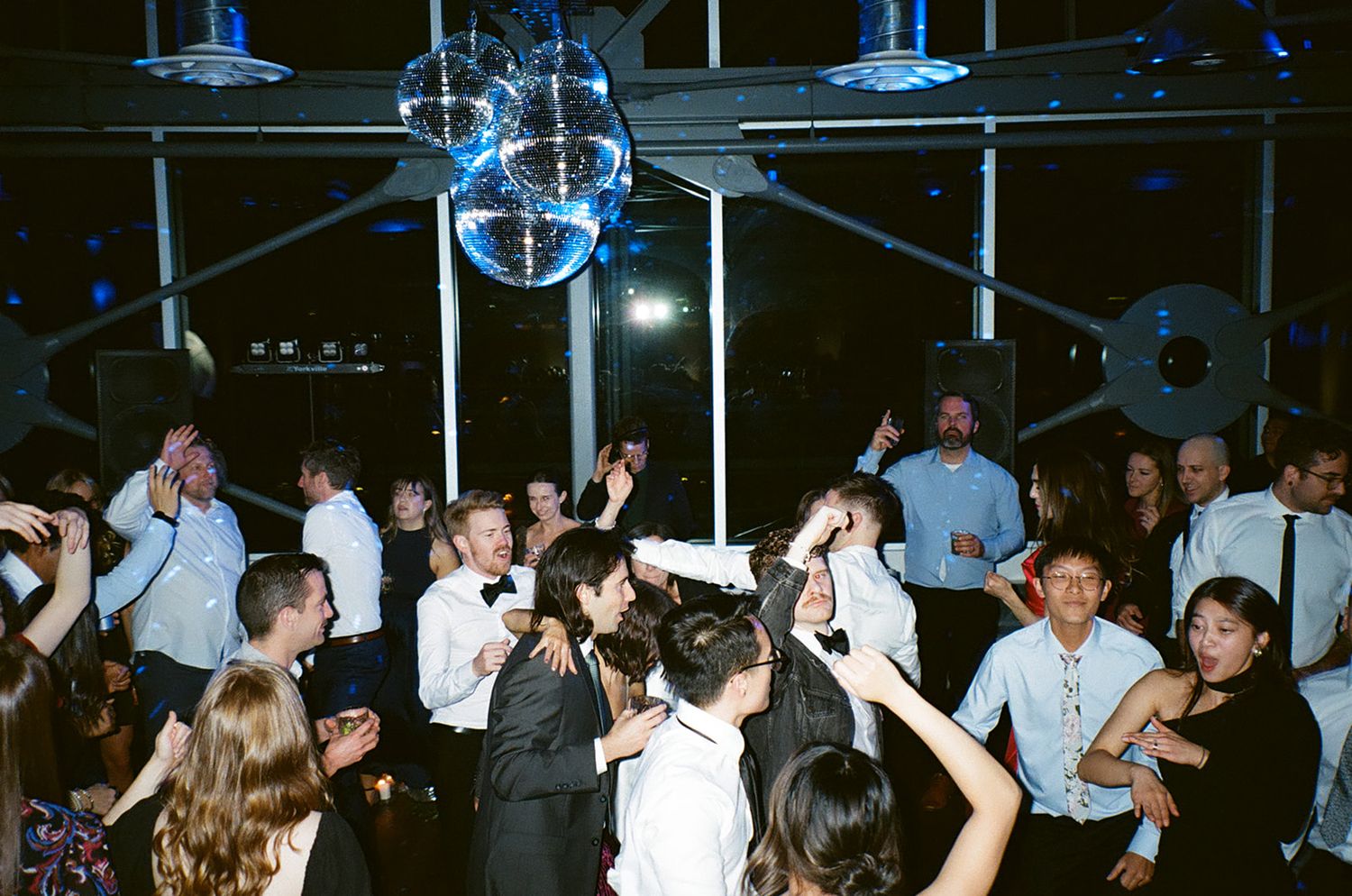 Large disco ball hangs over crowded dance floor at wedding reception.