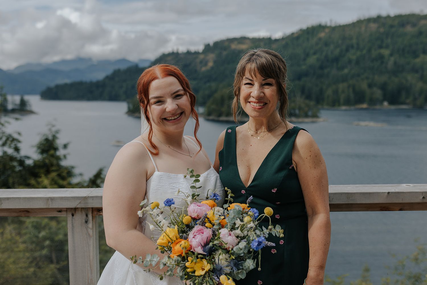 Celebratory wedding photos taken on wooden deck with beautiful lake and mountain scenery.