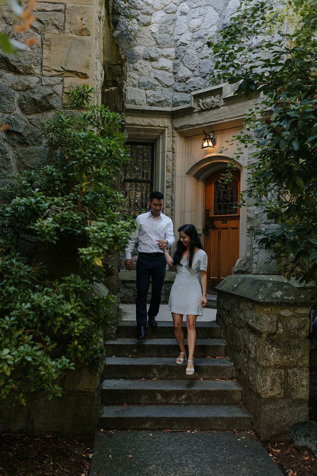 A couple descends stone steps outside a historic building with rustic architecture.
