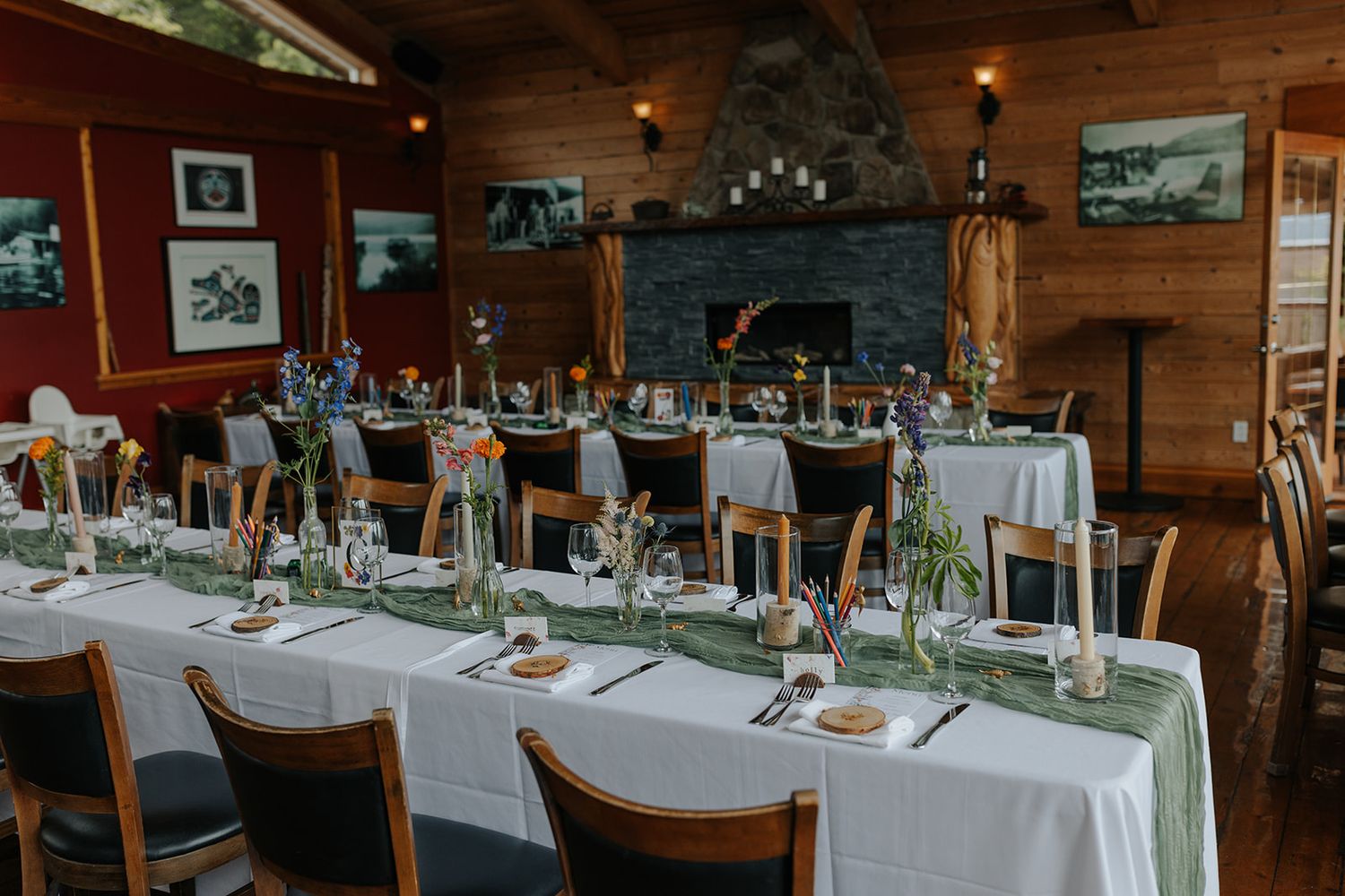 Elegant wedding reception setup in a rustic lodge with stone fireplace and white tablecloths.