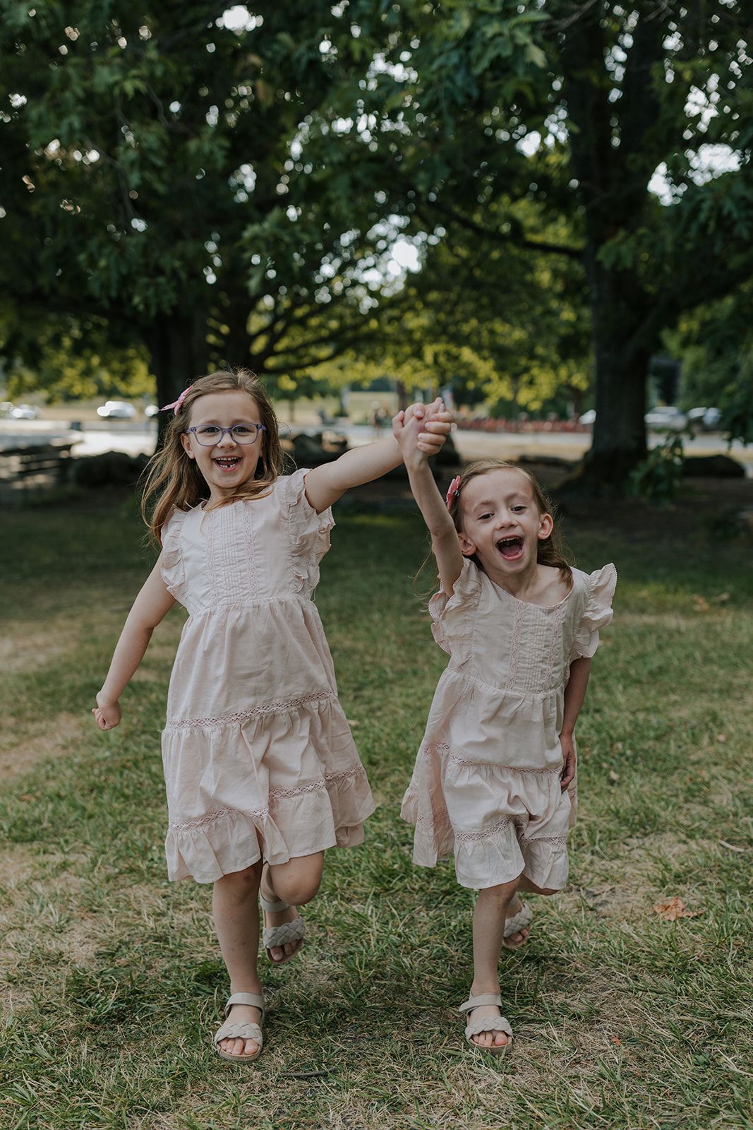 Two children in matching light dresses running and playing joyfully on grass.