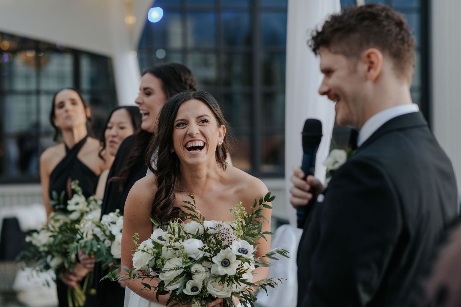 Wedding party members share joyful laughter during formal photos indoors.