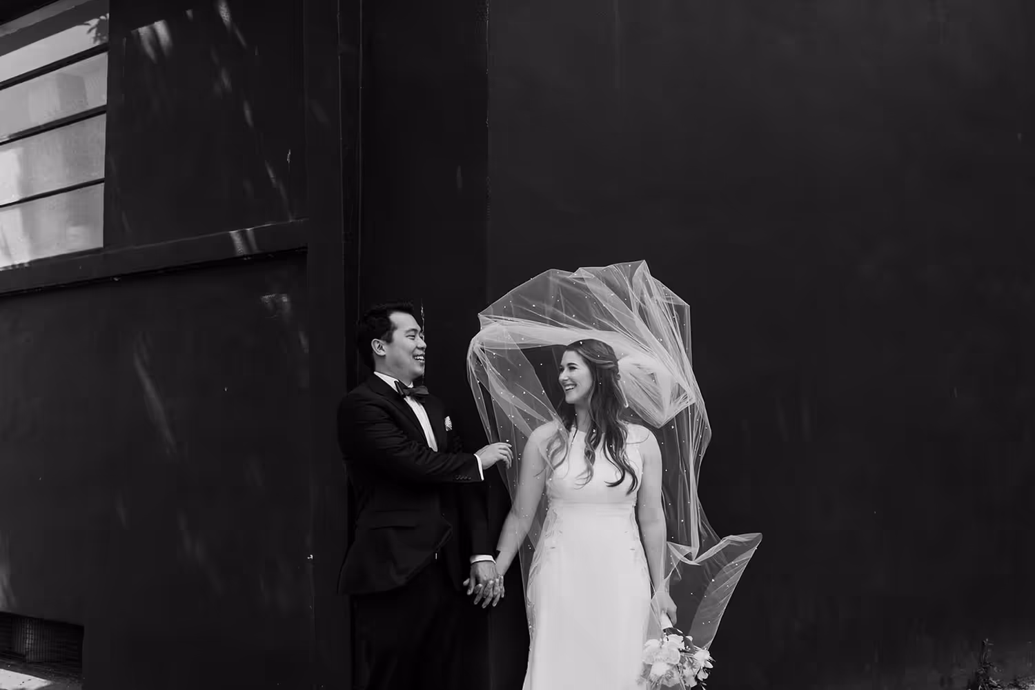 candid black and white image of a couple getting married in the city. veil blows artfully across the brides face