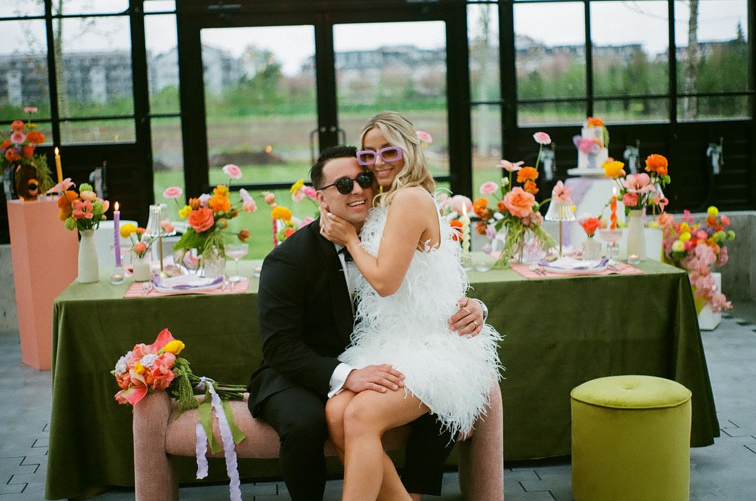 Wedding reception in a bright greenhouse venue with colorful floral arrangements and table settings.