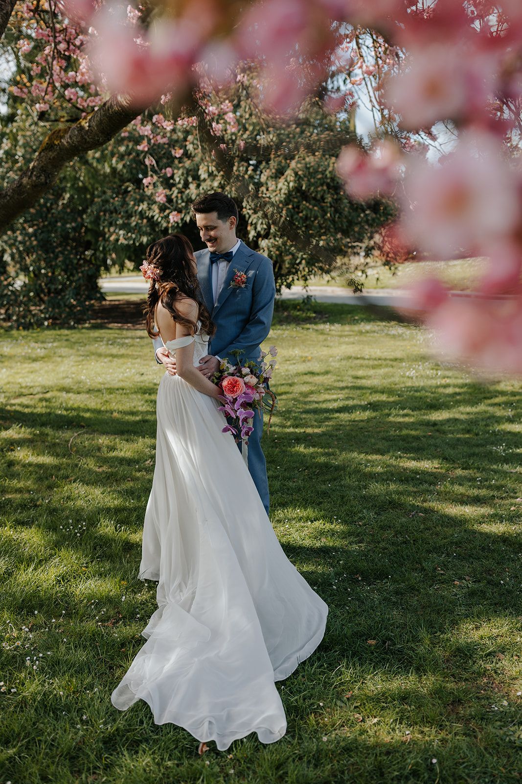 Couple walks through blooming cherry blossoms during spring wedding photoshoot.