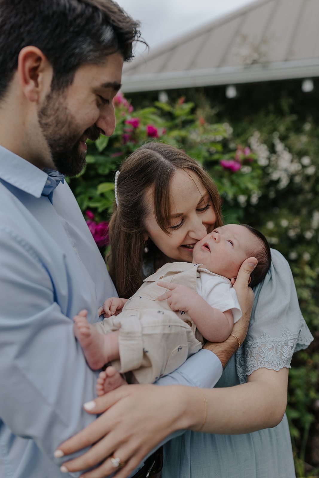 Outdoor family portrait session with baby among blooming flowers and greenery.