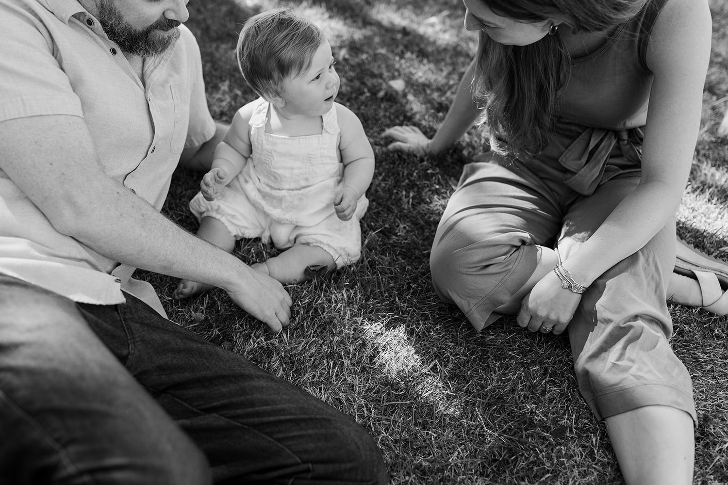 A family sits together on grass during an intimate black and white outdoor photoshoot.