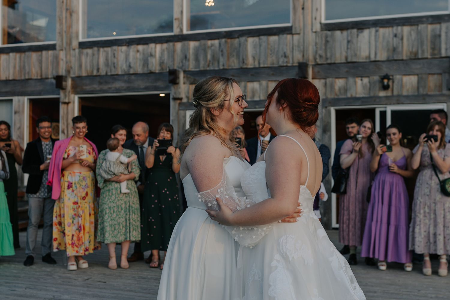 Wedding guests gather on a rustic wooden deck during a sunset celebration.