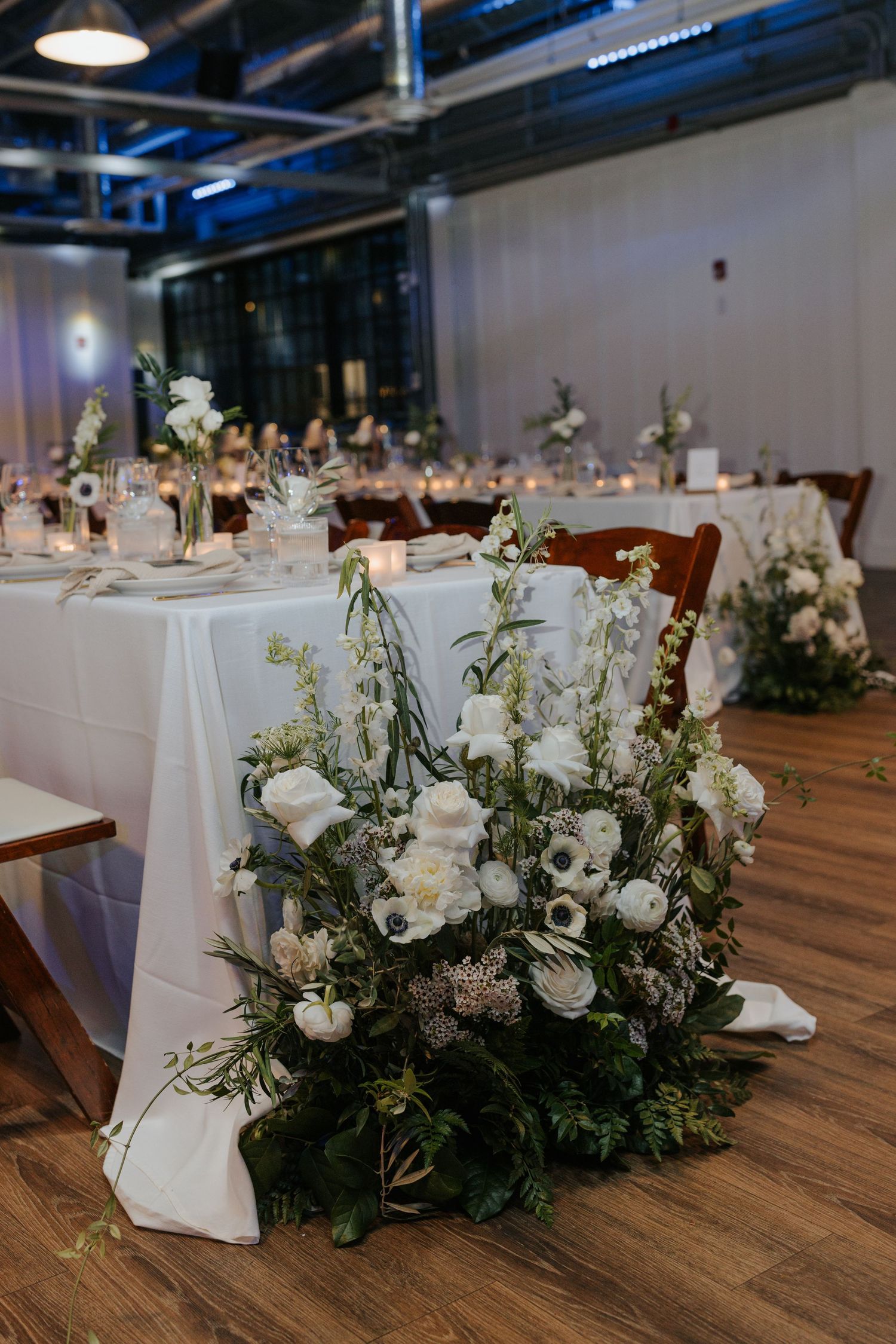 Elegant wedding reception setup with white linens and floral centerpieces in modern venue.