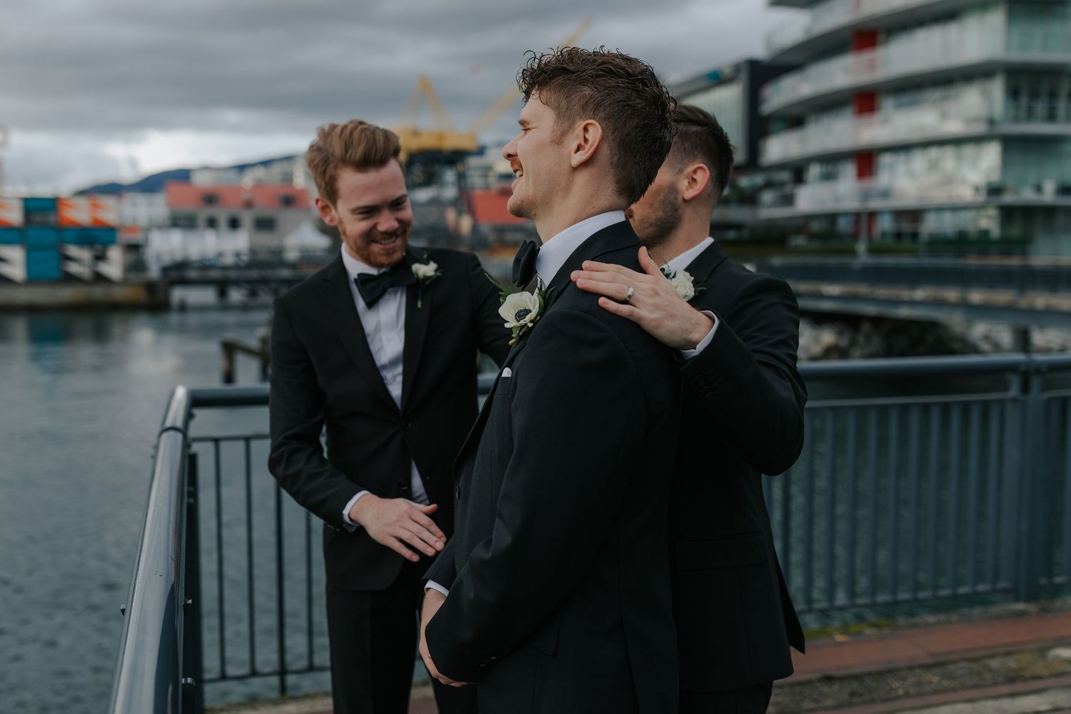 Two people share a candid moment while walking along a waterfront boardwalk on an overcast day.