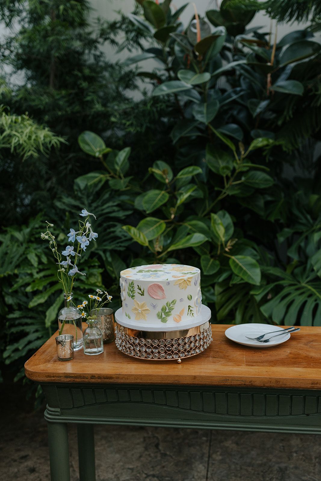Wedding cake decorated with fresh flowers displayed on wooden table in garden setting.