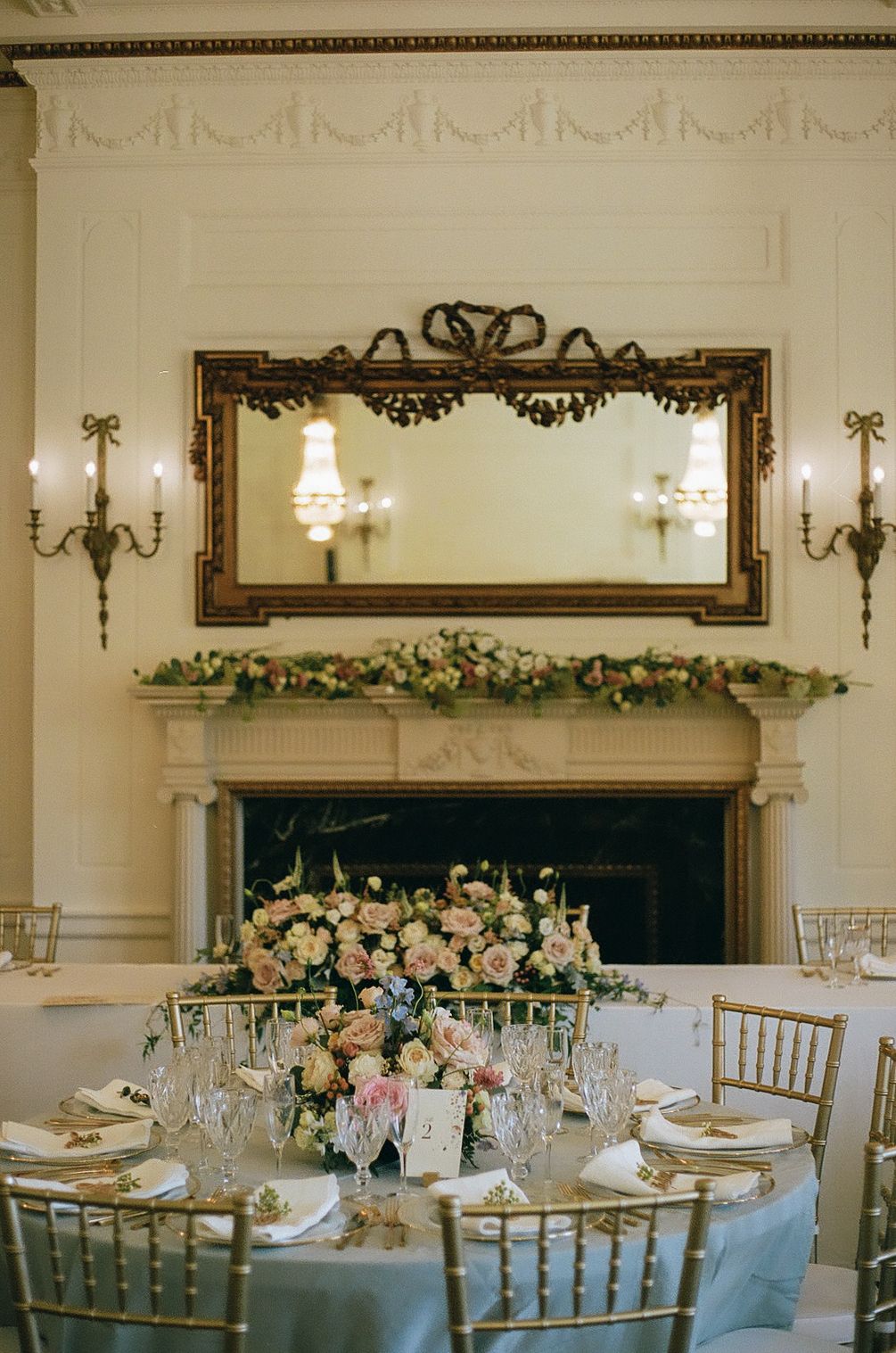 Elegant wedding reception table setting with ornate mirror and floral centerpiece.