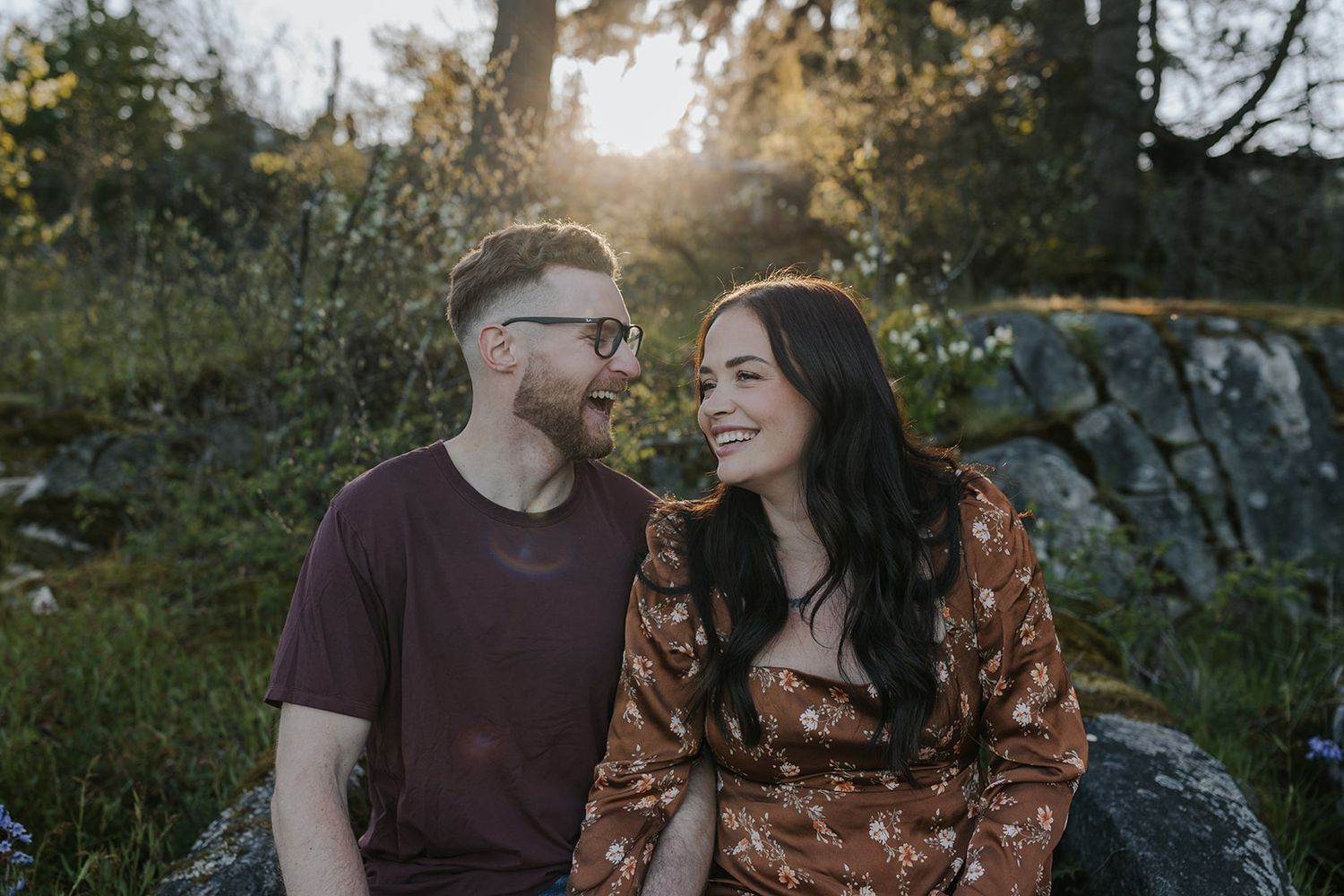 A couple shares a tender moment together while sitting on rocks during golden hour sunset.