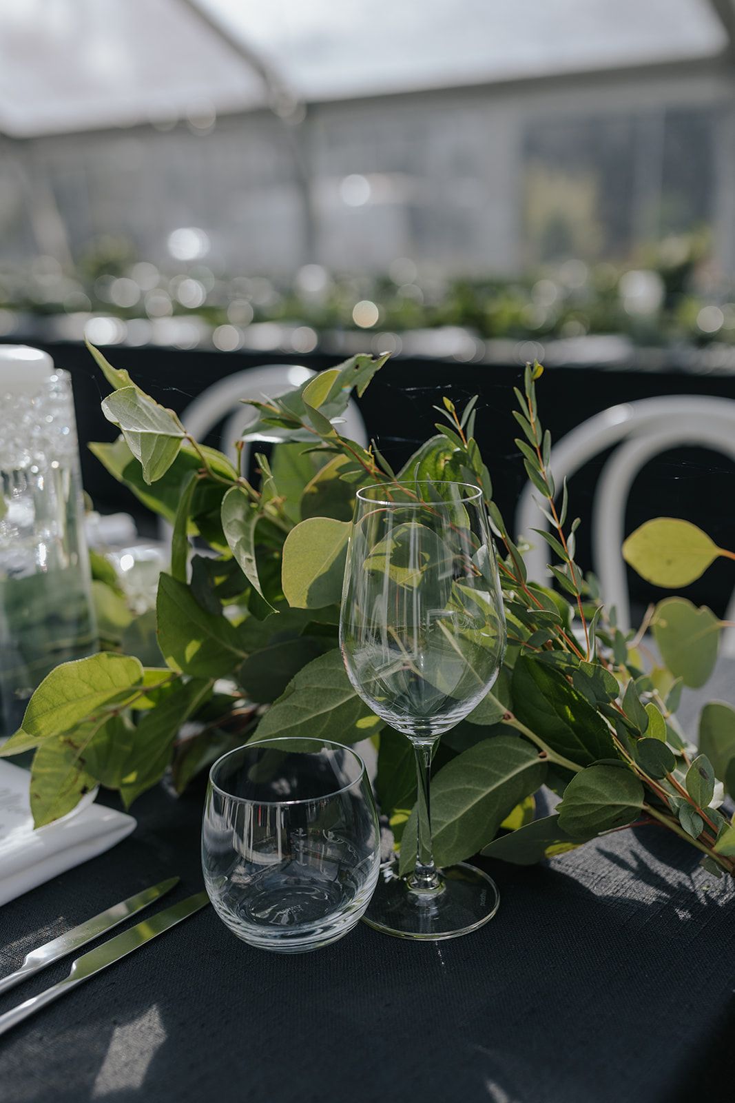 Elegant table setting with green foliage and wine glasses on black tablecloth.