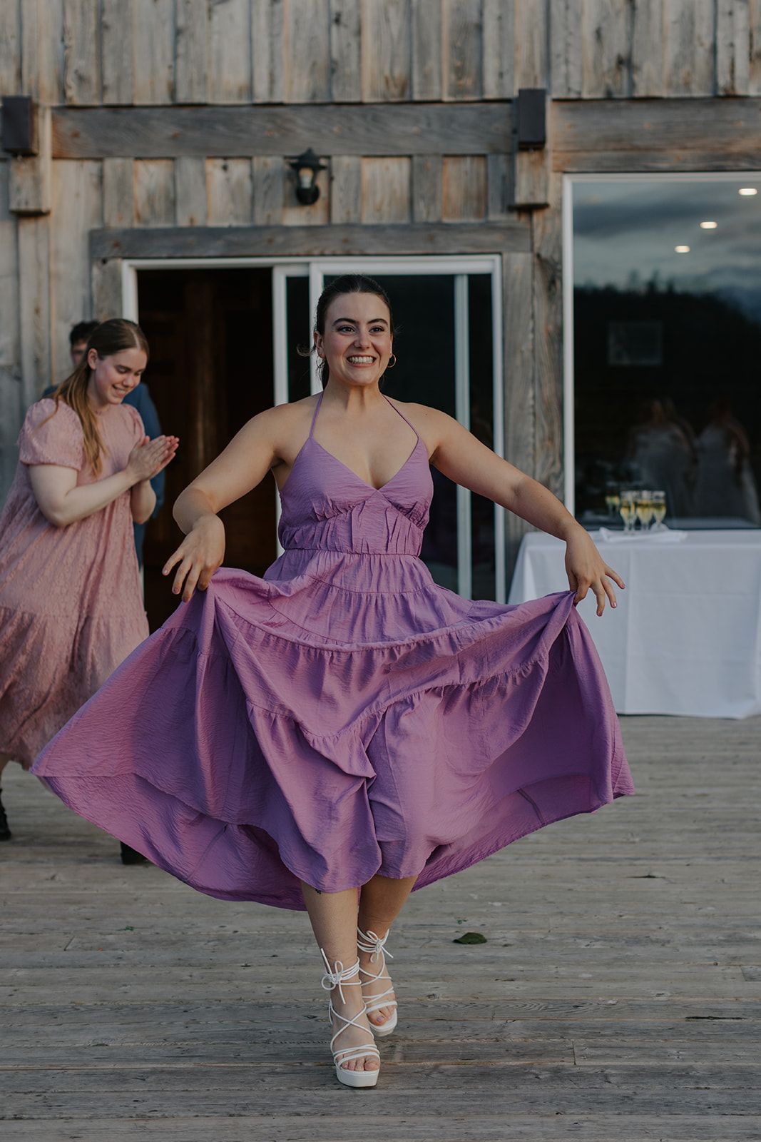 A person in a purple dress twirls on a wooden deck with mountains in the background.