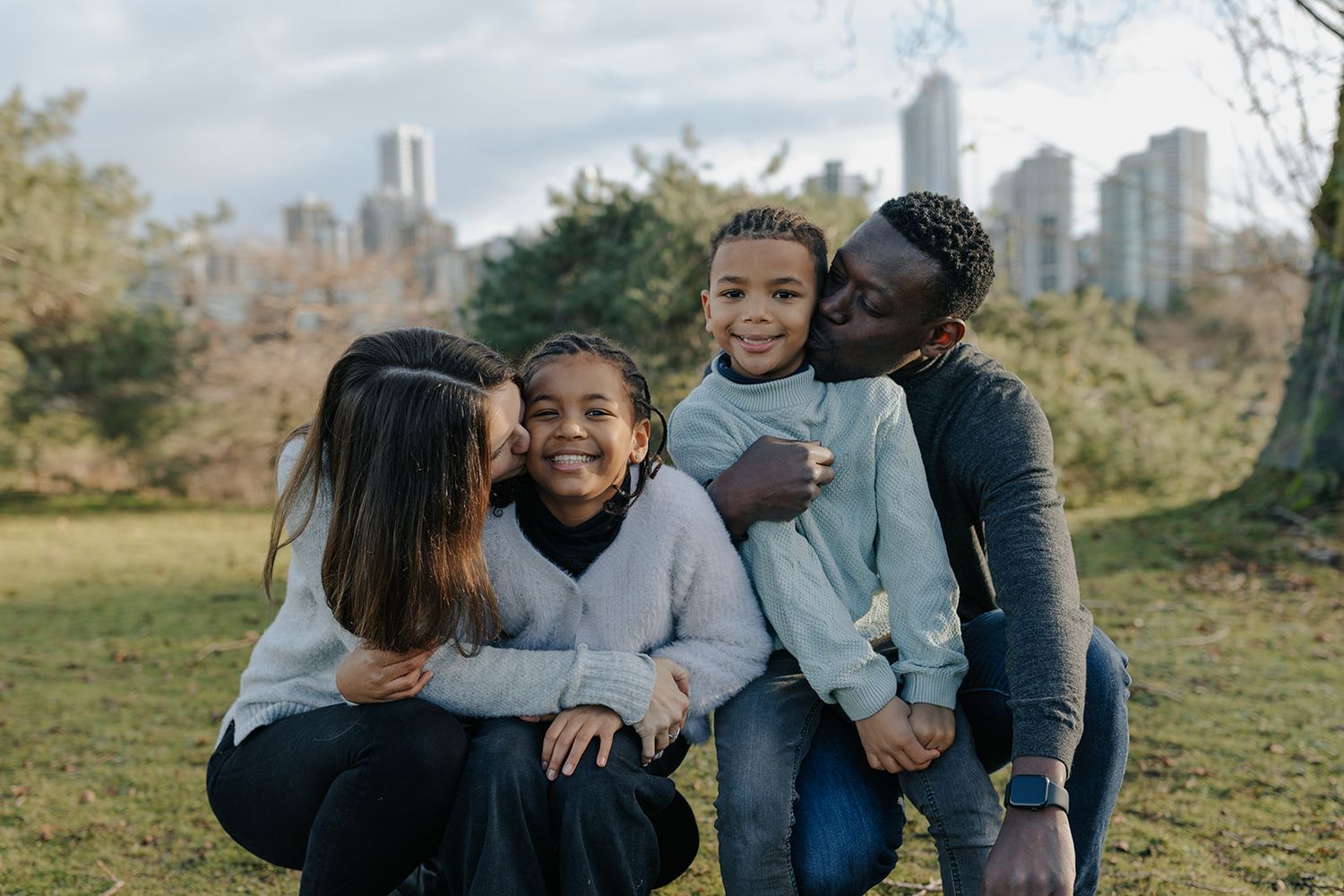 Family enjoying a sunny day together in a park with city skyline in the background.