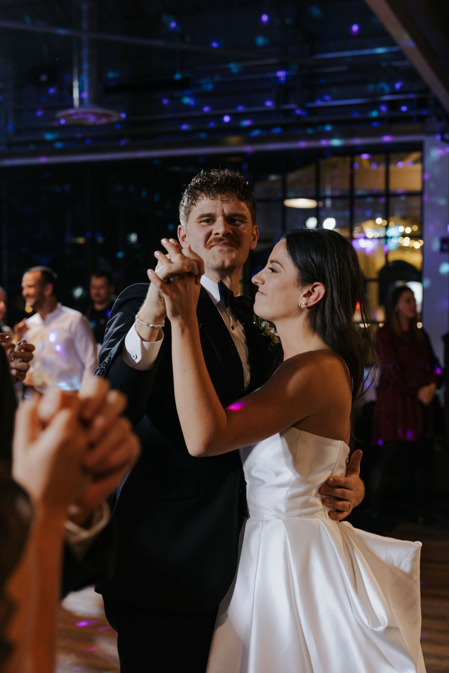 Wedding guests dancing together in a dimly lit reception venue with blue lighting.
