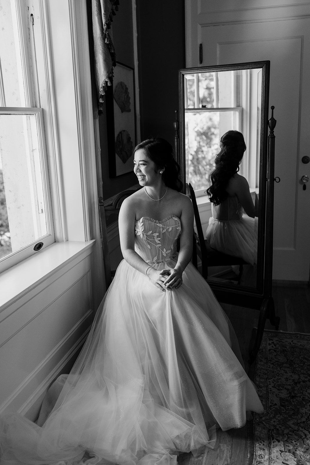 Black and white photo of flowing white wedding dresses near sunlit windows.