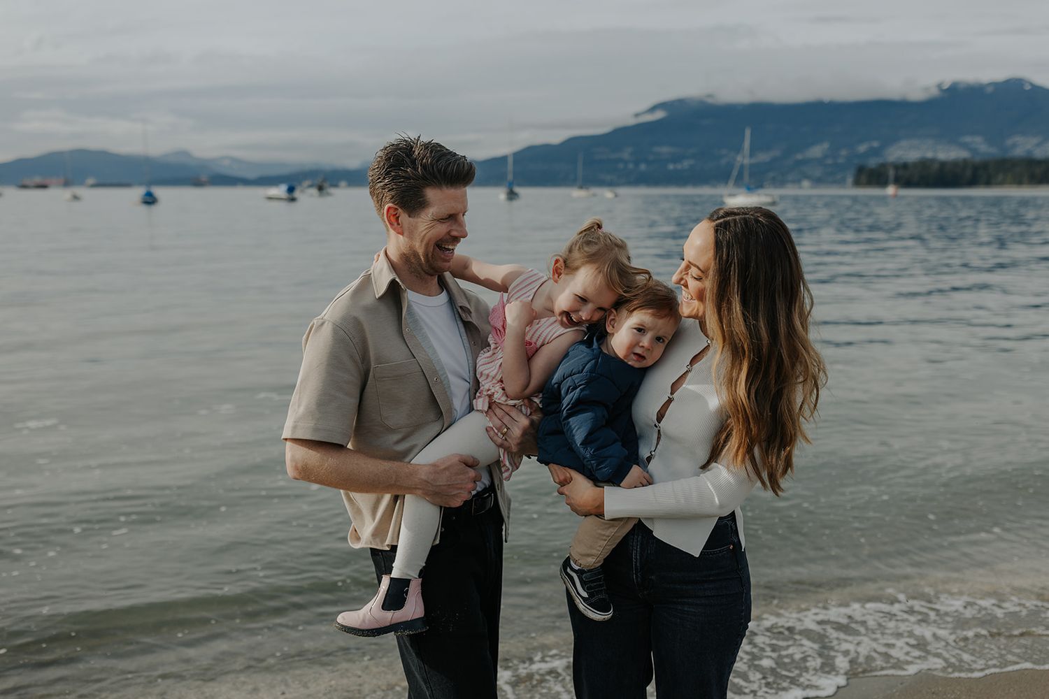 Family sharing a tender moment together at the beach with sailboats in the background.