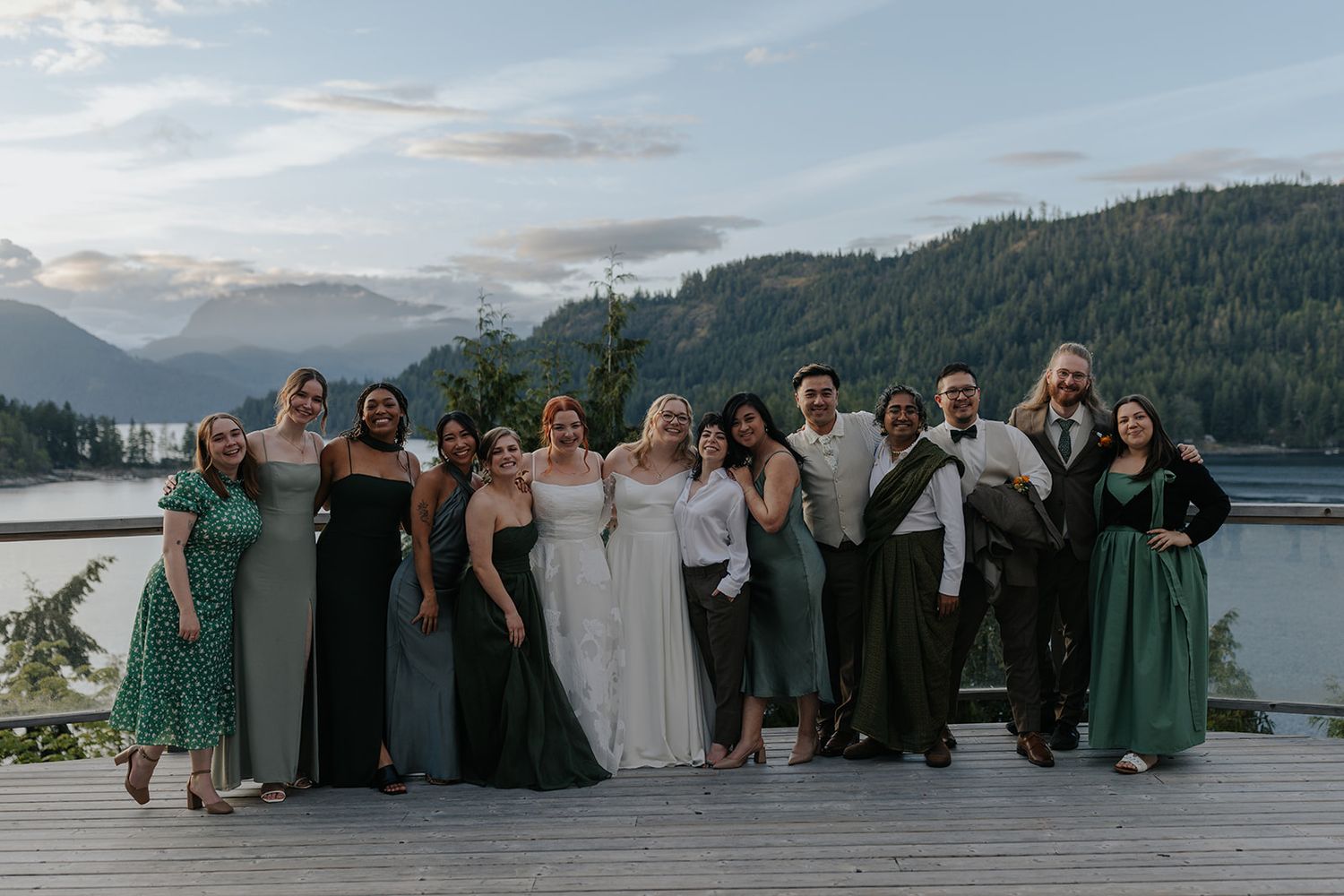 Wedding party members sit together on a deck with a beautiful mountain and lake backdrop.