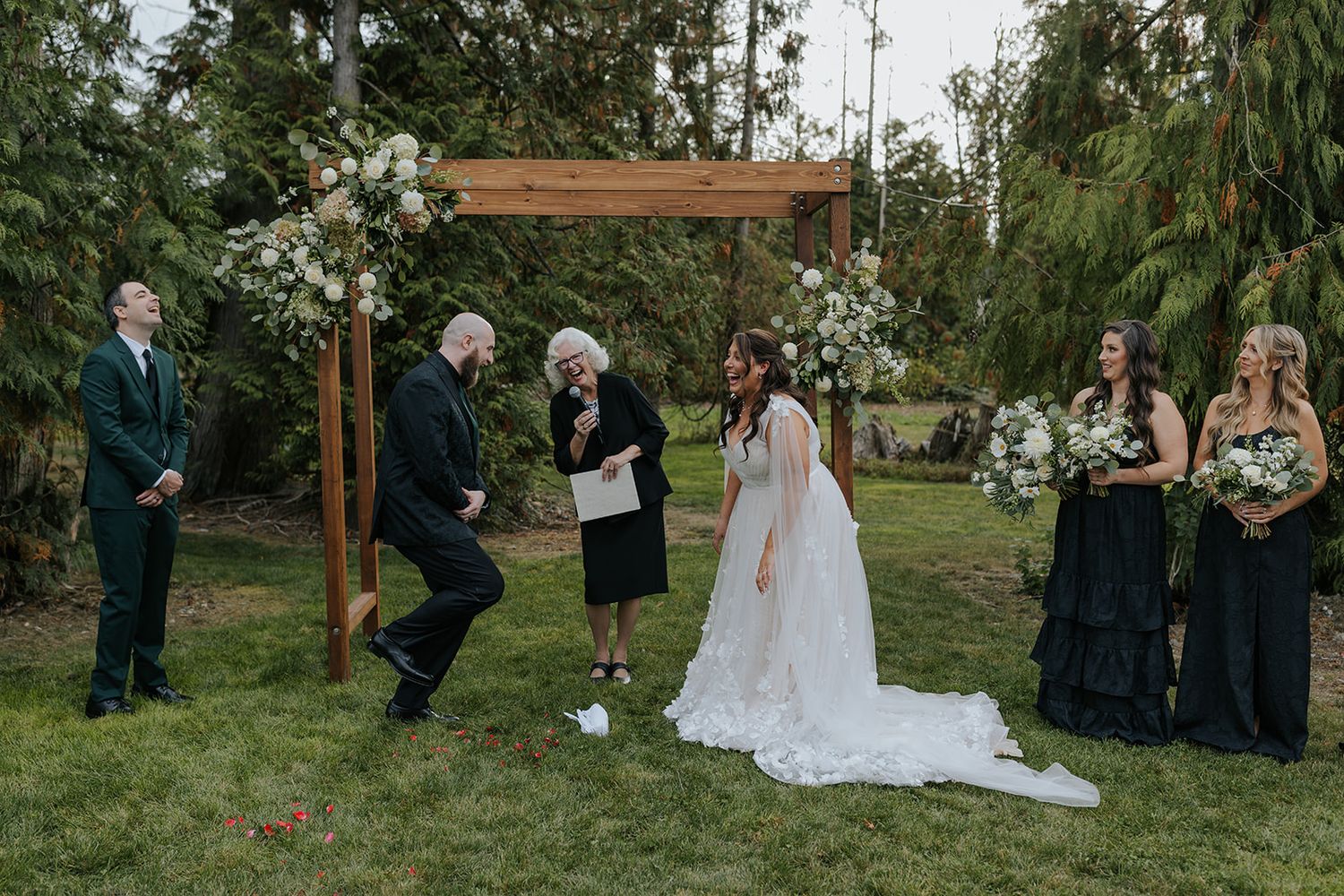Outdoor wedding ceremony setup with wooden cross and guests gathered in a garden setting.