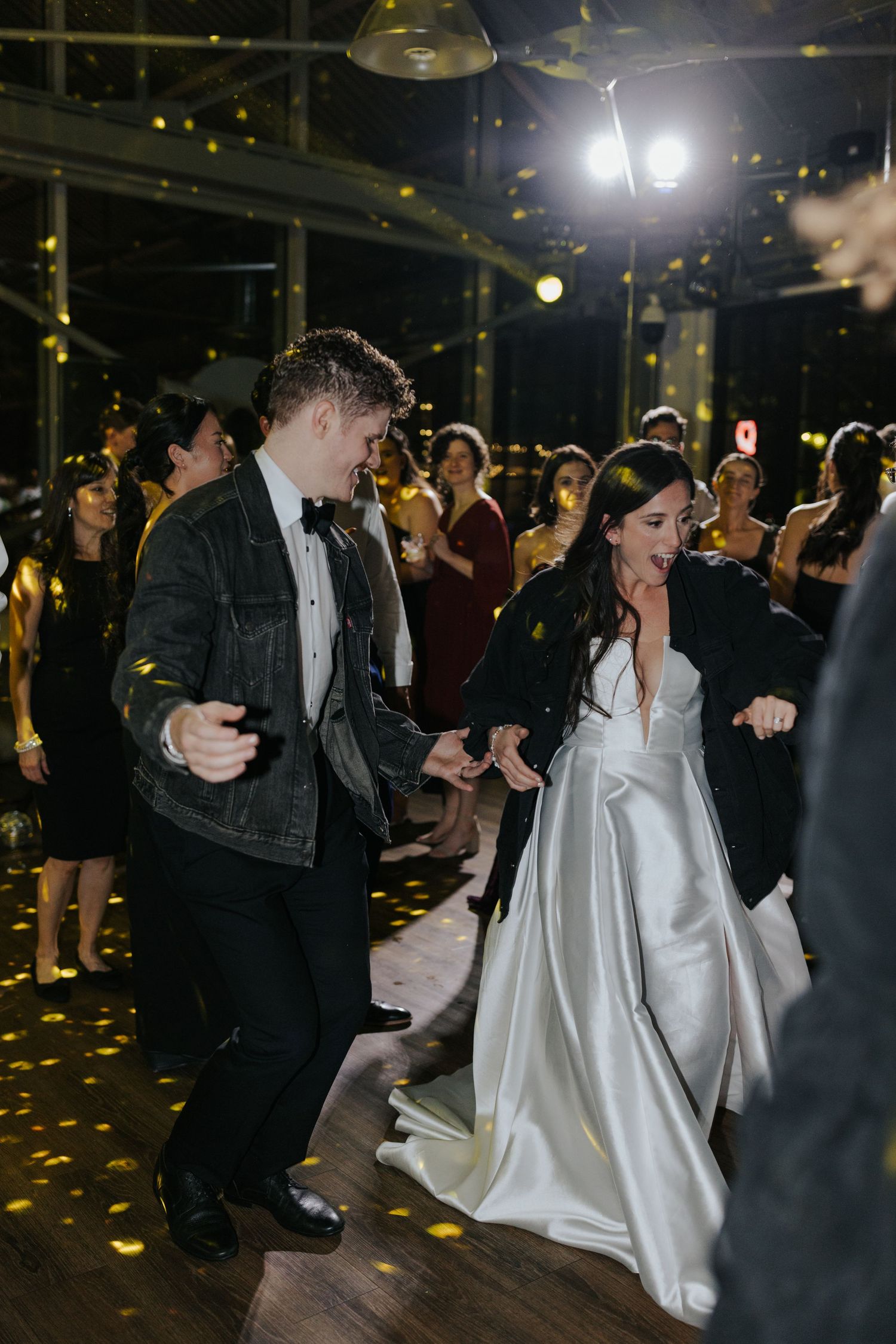 Wedding guests dance together under dim lighting and golden confetti at the reception.