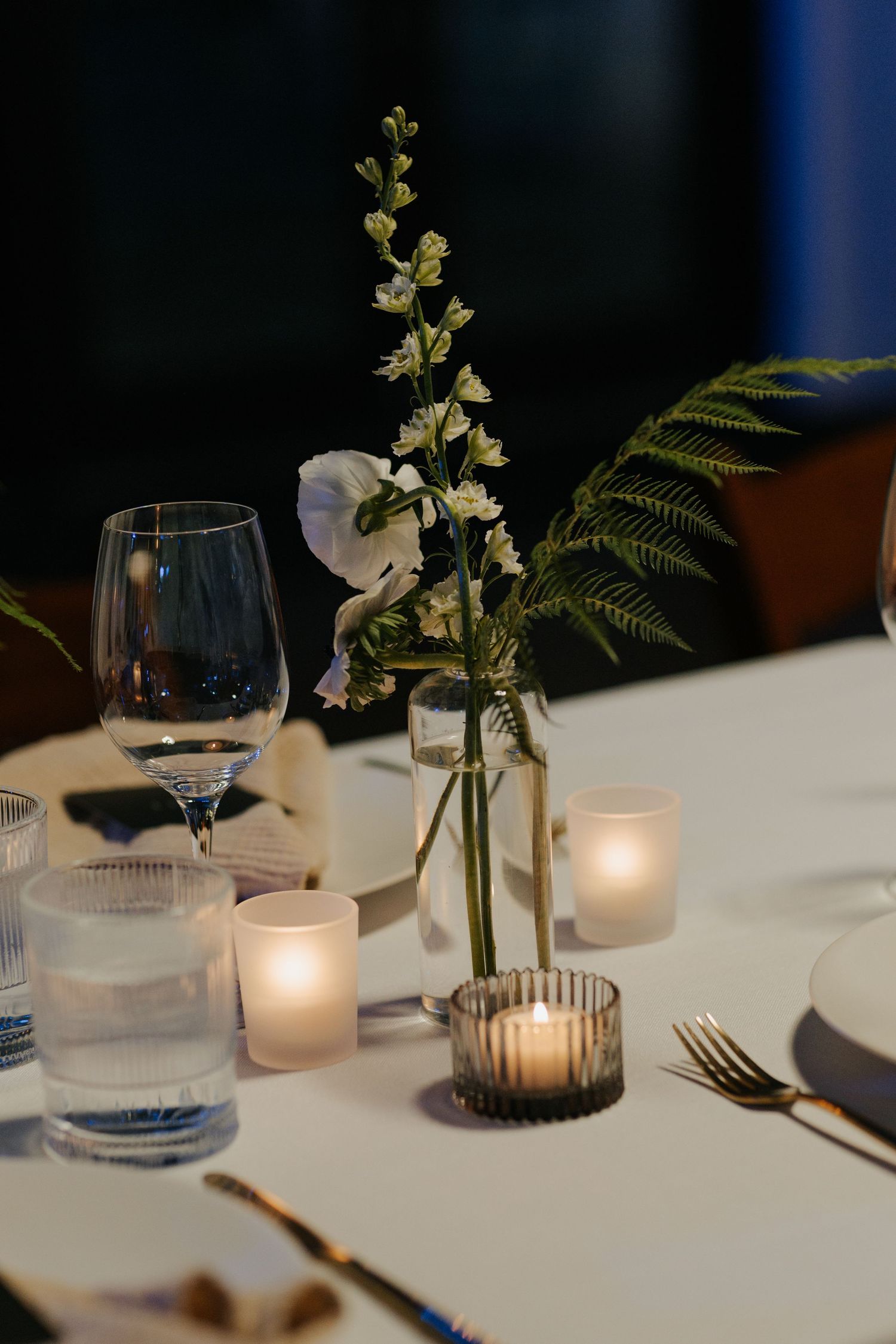 Elegant table setting with white candles, delicate floral arrangements and wine glasses.