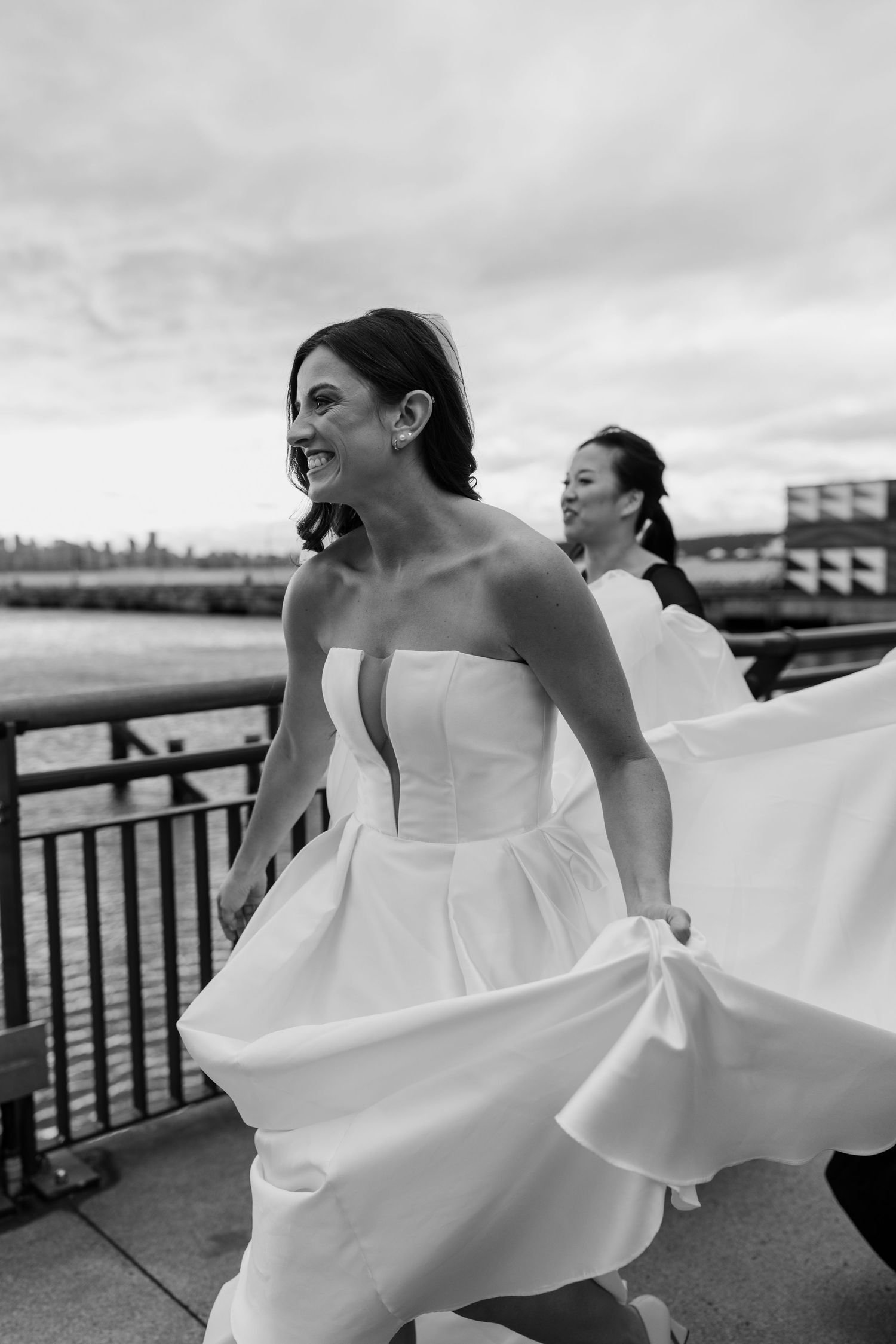 A joyful moment captured of a bride twirling in her white wedding dress on a waterfront boardwalk.