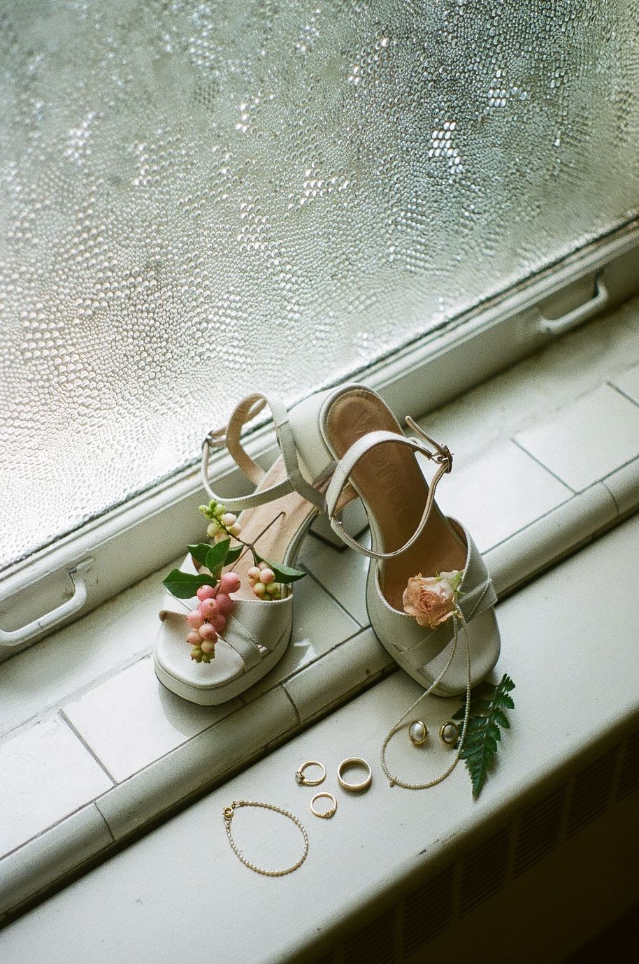 White bridal shoes displayed on a misty windowsill with delicate floral accents.